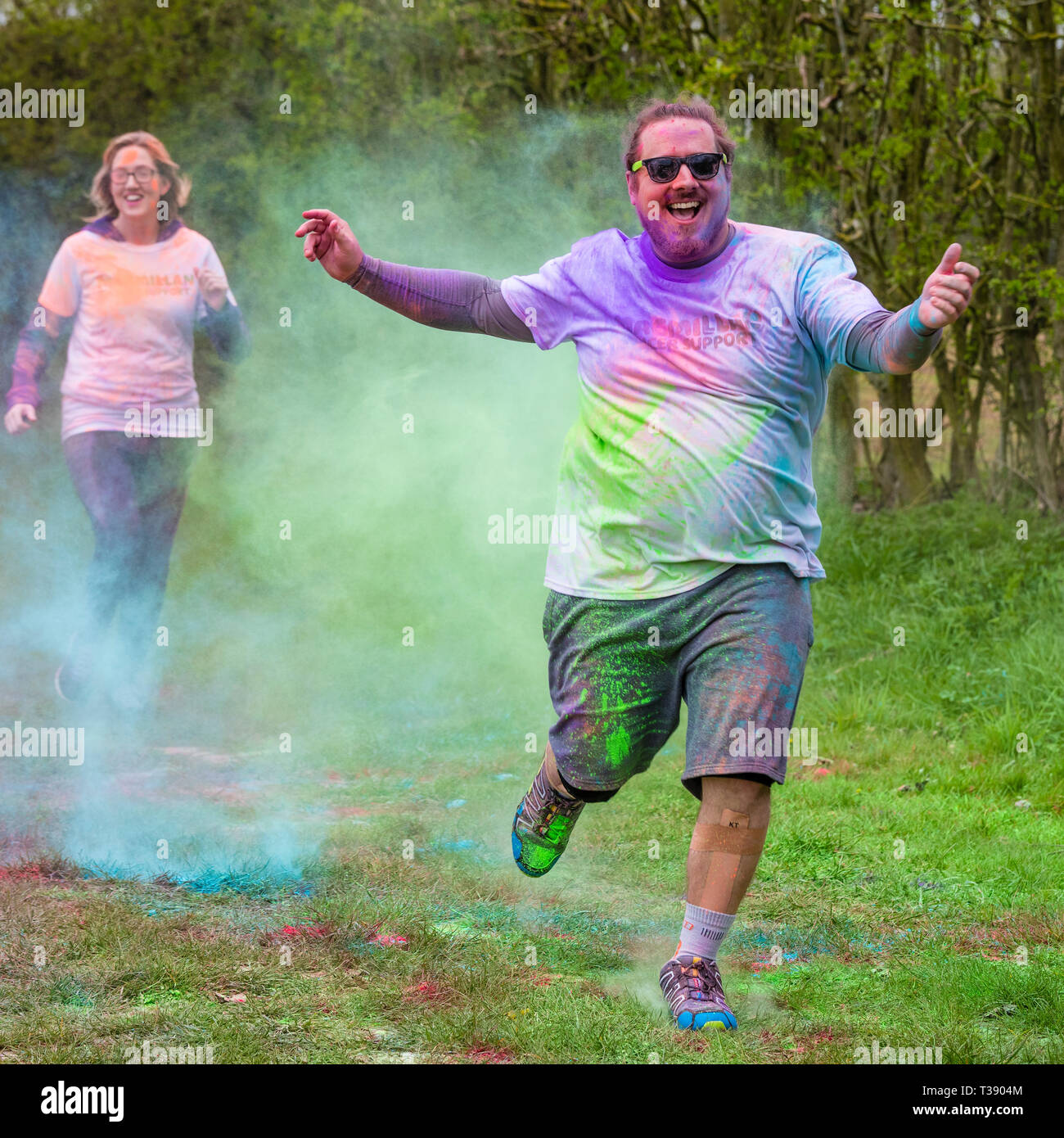 Grand homme de rire et de surpoids runner bras tendus se couvrir de peinture sur Macmillan Cancer 5K fun run de couleur. Banque D'Images