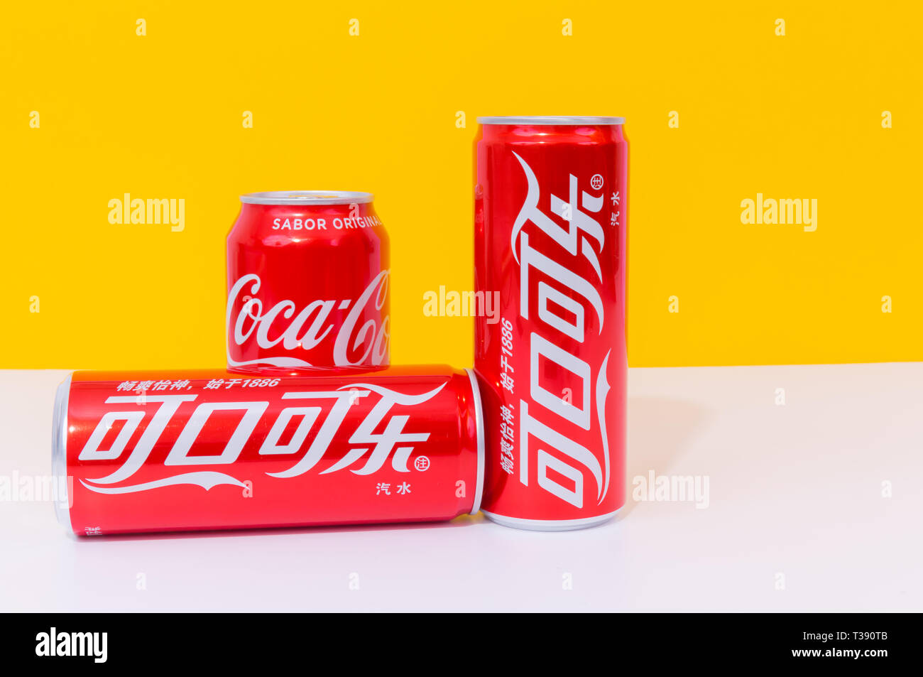 Peniscola , Paris, France - 07 avril 2019 : trois canettes de Coke, deux écrits en chinois, des boissons isolé sur fond jaune. Le non-alcoolique b Banque D'Images