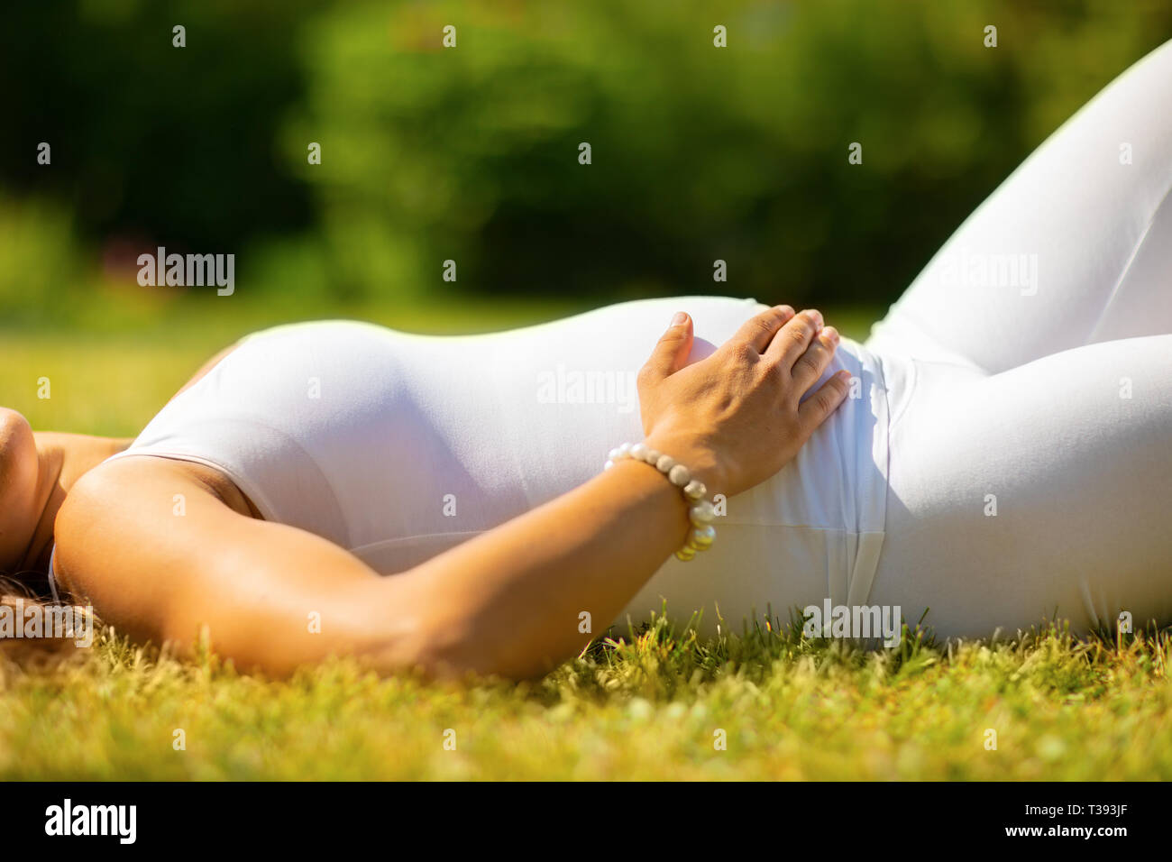 Close-up de la belle femme enceinte dans des vêtements blancs portant sur l'herbe Banque D'Images