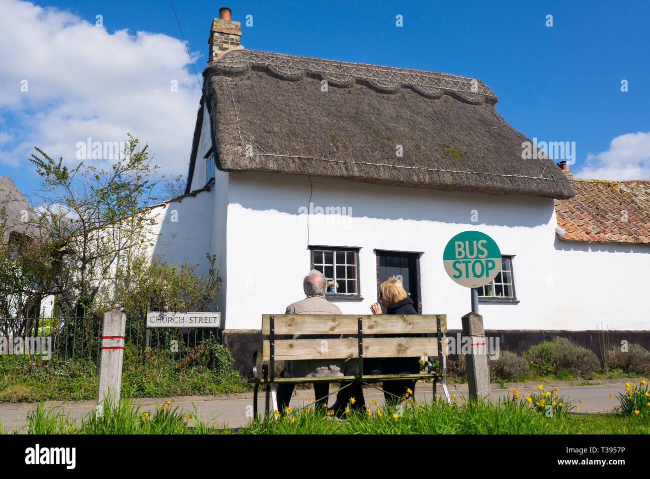 Newton, Cambridge, England, UK - Mars 2019 : old couple assis sur un banc en bois dans un village de bus avec cottage traditionnel britannique Banque D'Images
