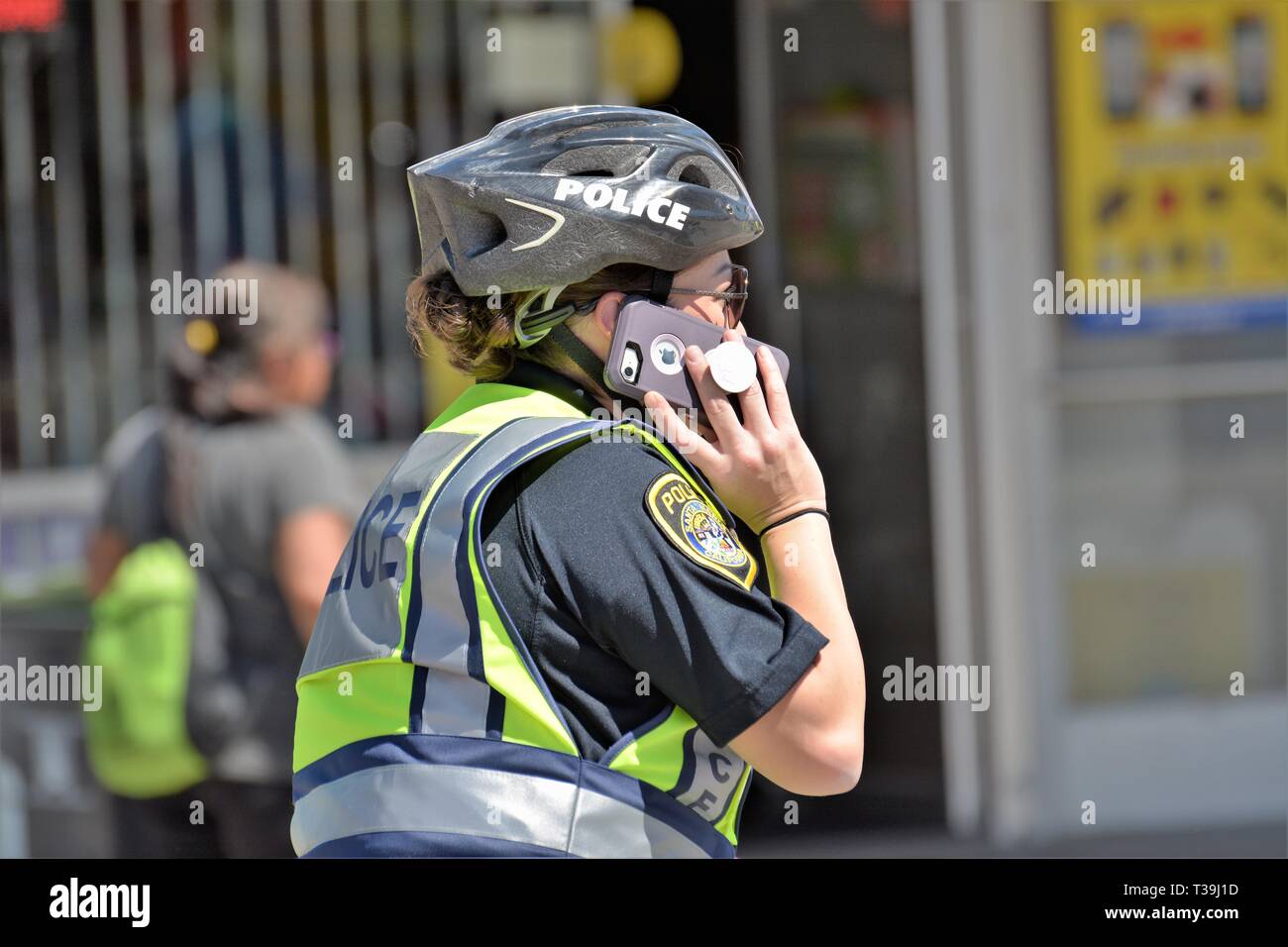 Femme policier sur téléphone cellulaire comme elle est sur patrouille à pied avec casque et gilet de sécurité jaune Banque D'Images