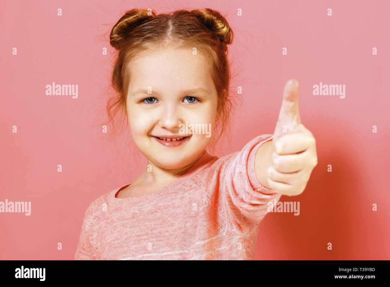 Closeup portrait of a cute joli petit enfant girl showing thumb up sur fond rose. Banque D'Images