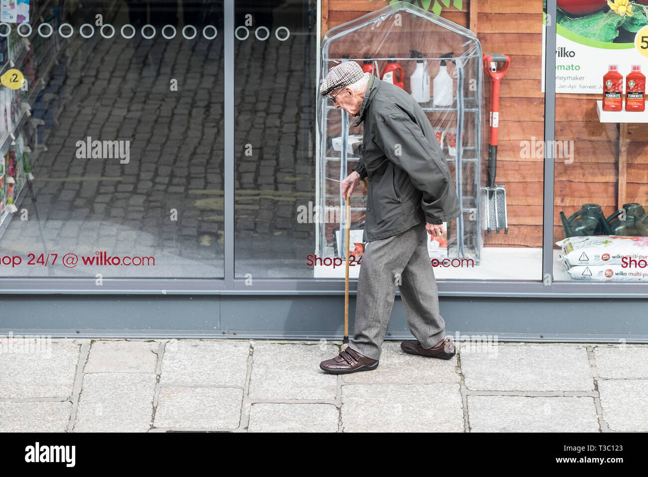 Un vieux monsieur se pencha sur son stick marchant le long d'une chaussée. Banque D'Images
