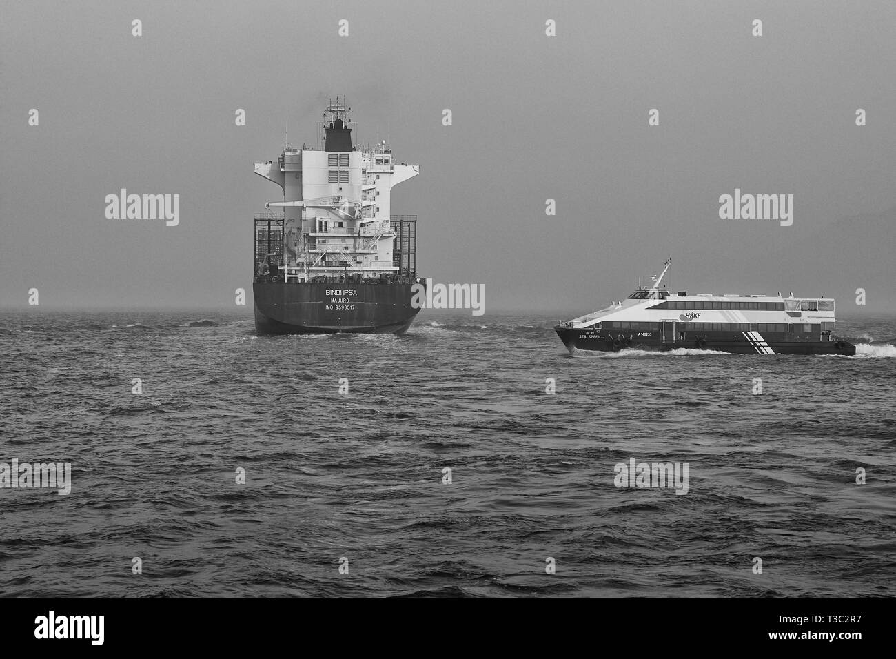 Photo en noir et blanc du navire porte-conteneurs, BINDIIPSA, sortant de l'Est, Canal Lamma Hong Kong. Un ferry rapide passant à l'arrière. Banque D'Images