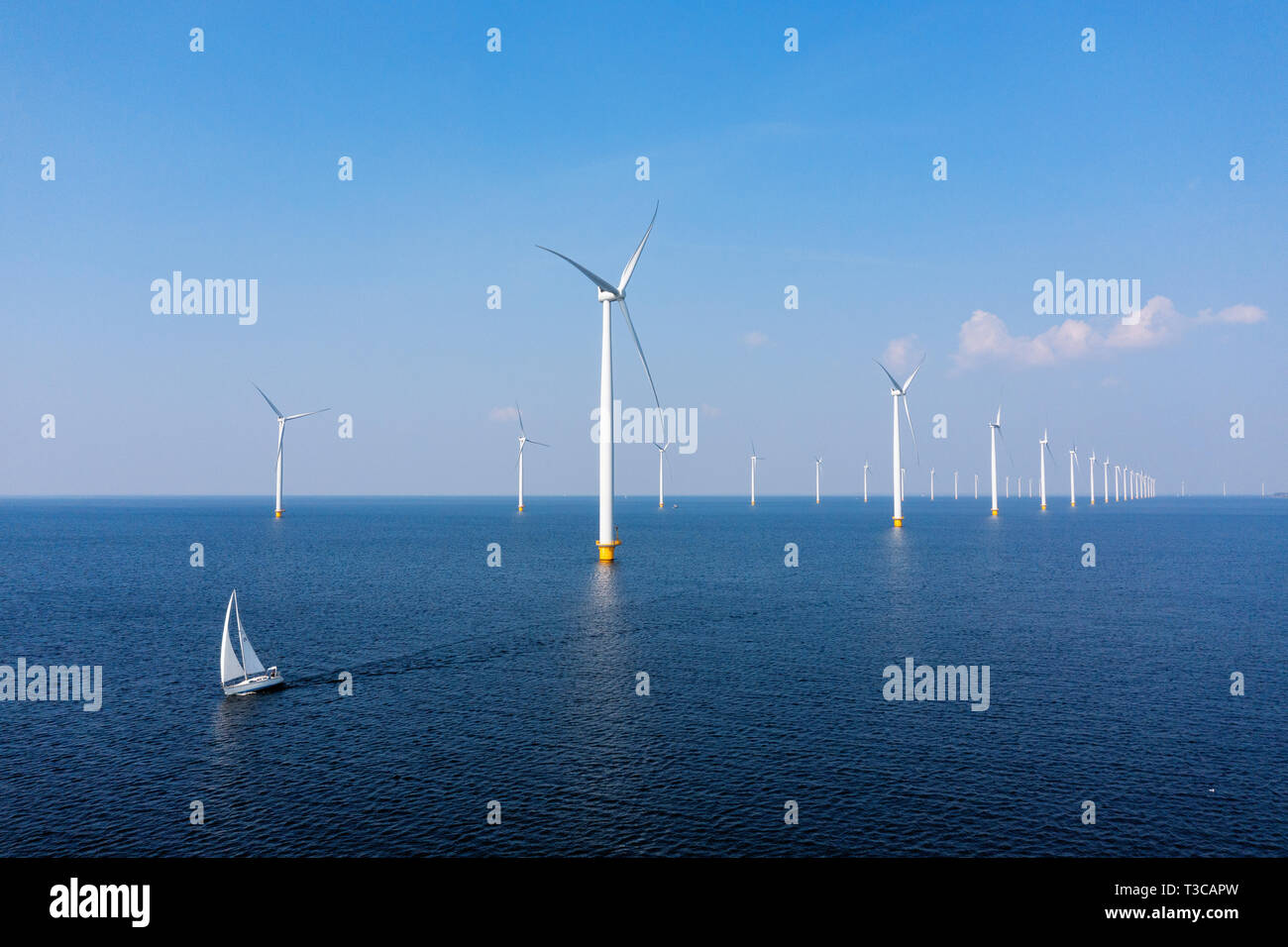 Éoliennes dans une mer bleue sur une journée ensoleillée avec un bateau à voile en passant par Banque D'Images