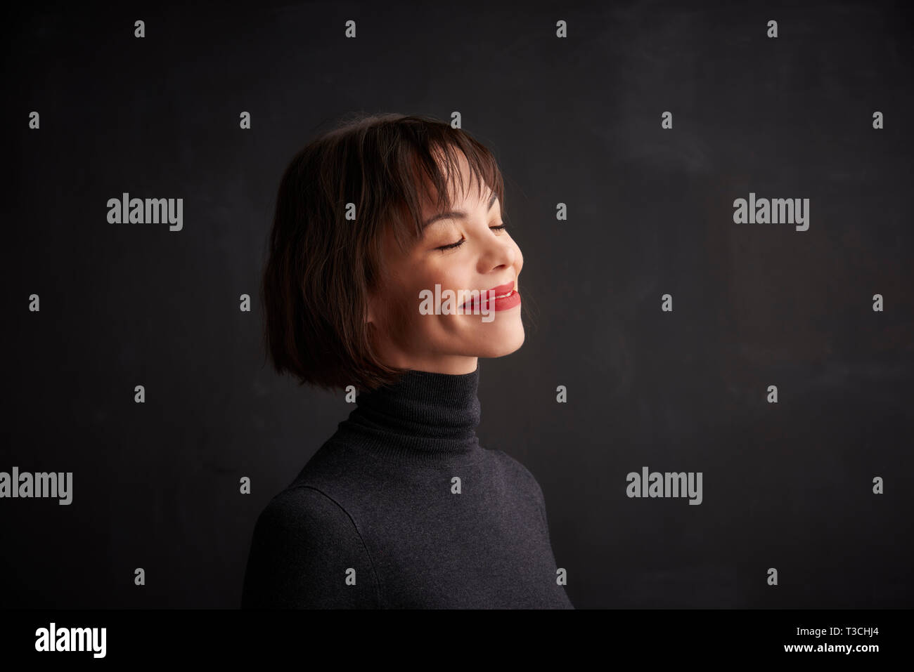 Studio head shot of woman wearing red lipstick and roll neck sweater tout en se tenant à l'bacgkround sombre. Banque D'Images