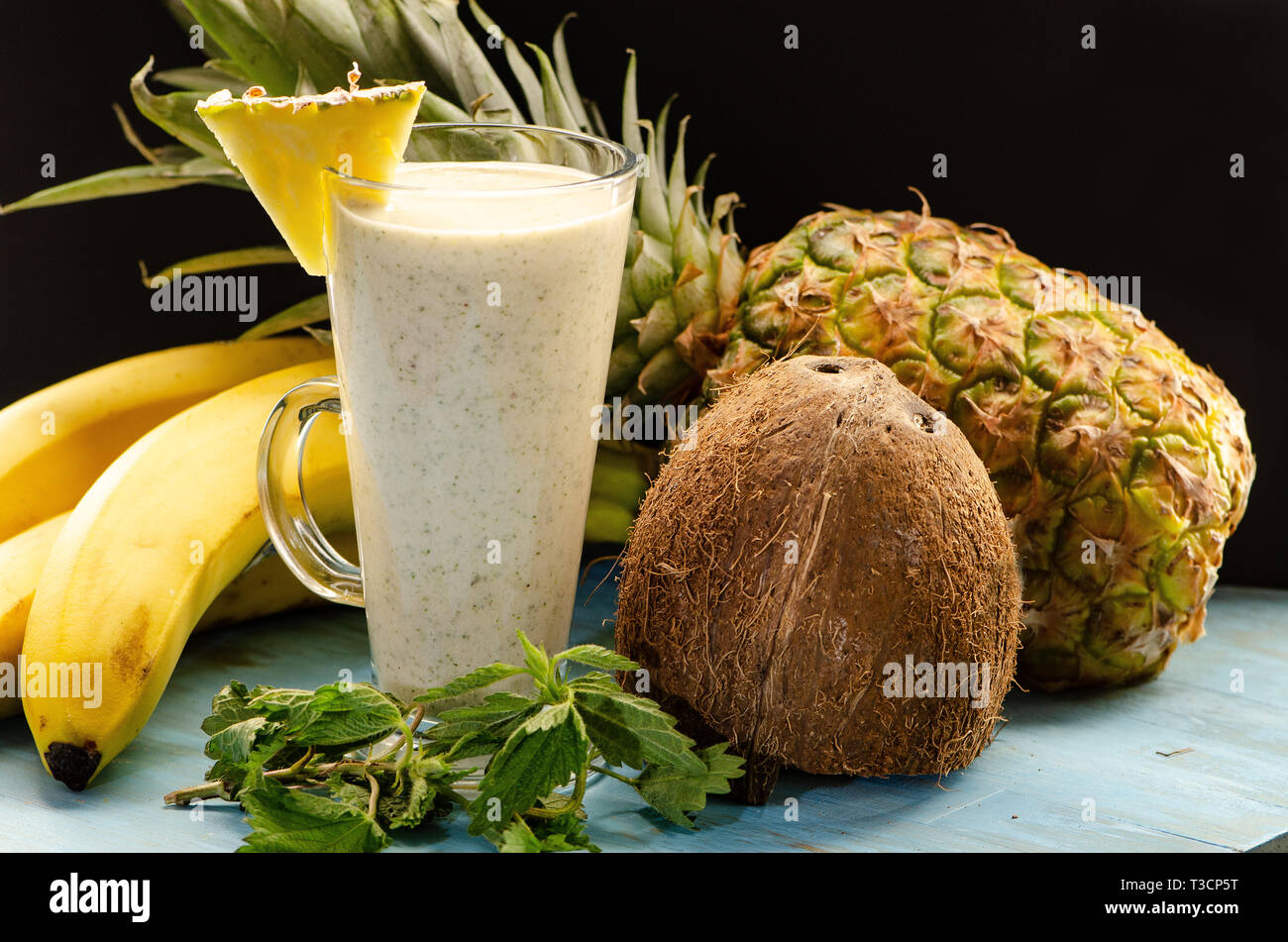 Smoothie d'ananas, les bananes, les orties et le lait de coco sur une planche en bois bleu clair Banque D'Images