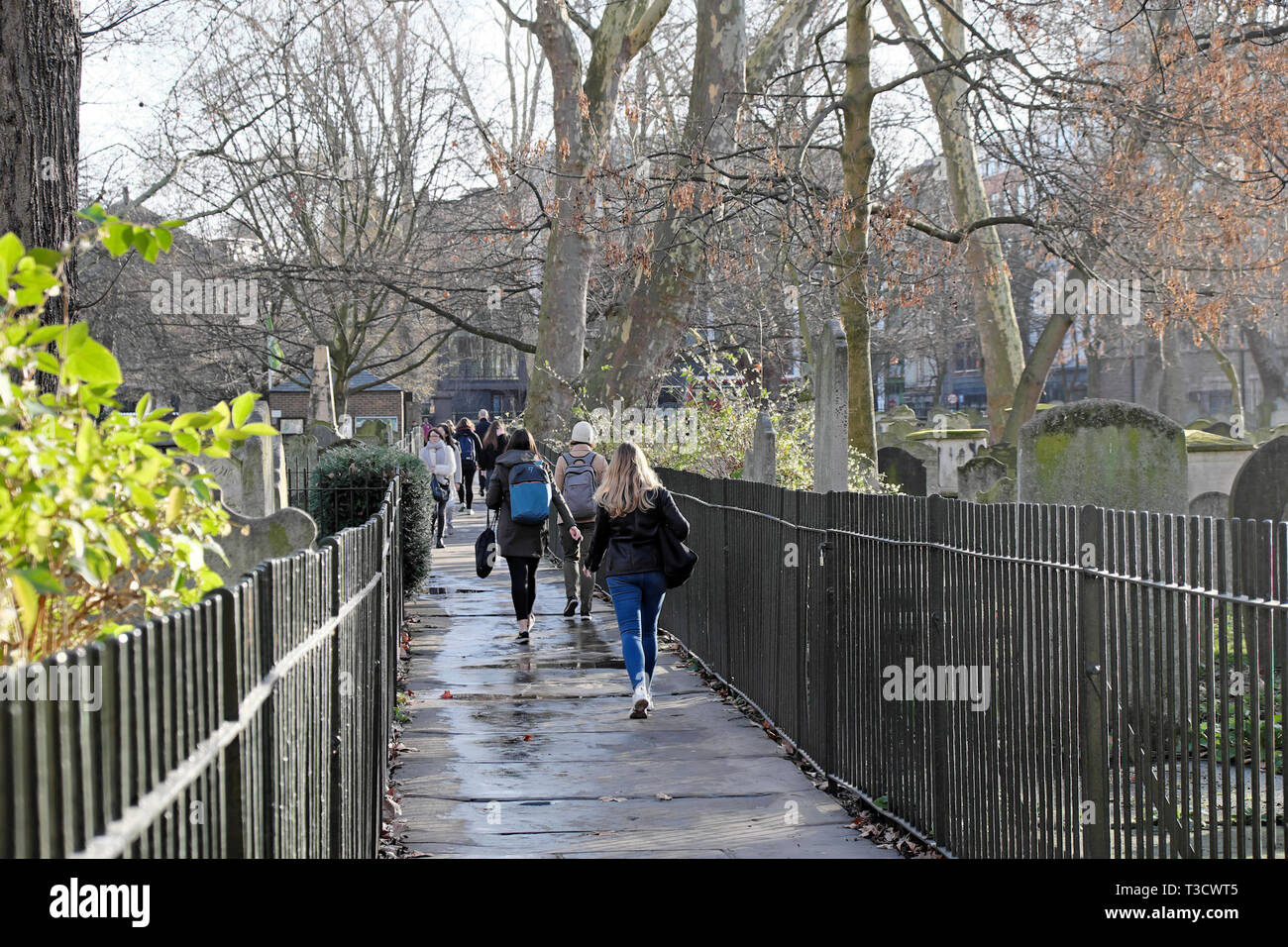 Les gens qui marchent au travail et à l'école le long d'un chemin à côté de pierres tombales dans le cimetière Bunhill Fields au début du printemps dans London EC1 England UK KATHY DEWITT Banque D'Images