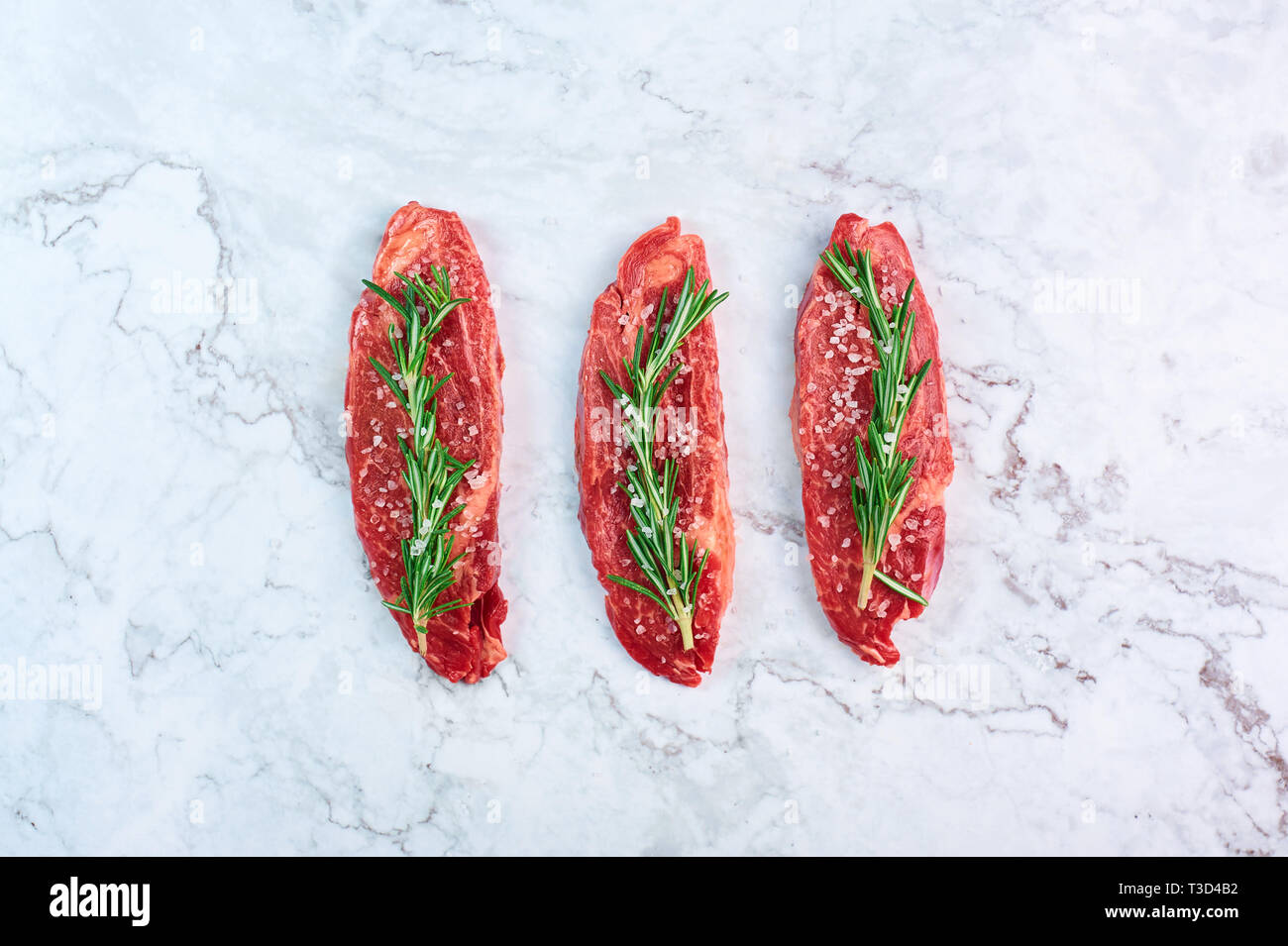 Les steaks de marbre brut vert avec Rosemary Branch et de sel de mer à l'arrière-plan en marbre blanc. Copy space Banque D'Images