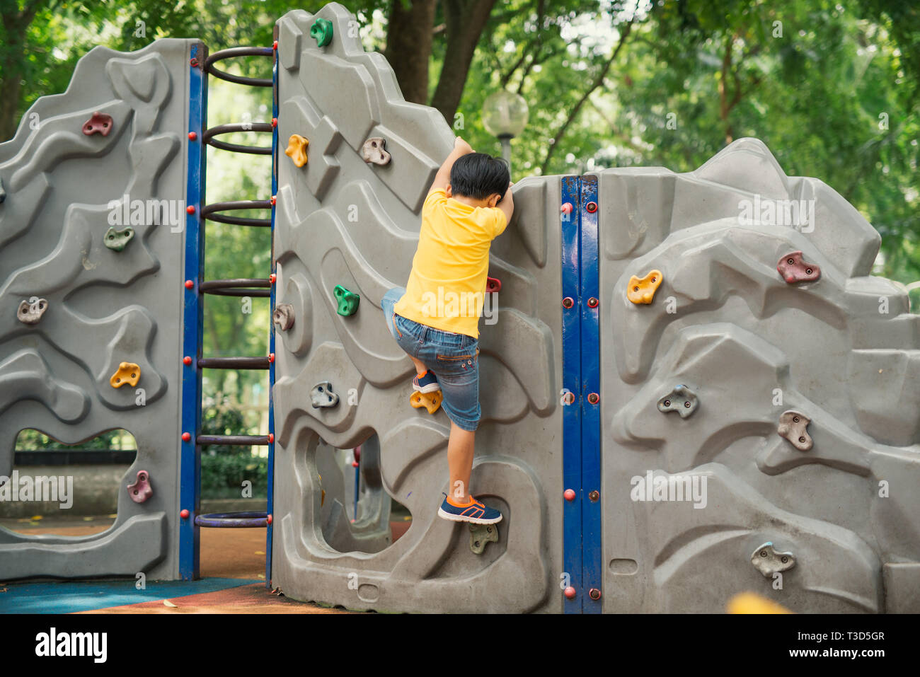 Petit garçon escalade sur le mur de roches à l'aire de jeux Banque D'Images