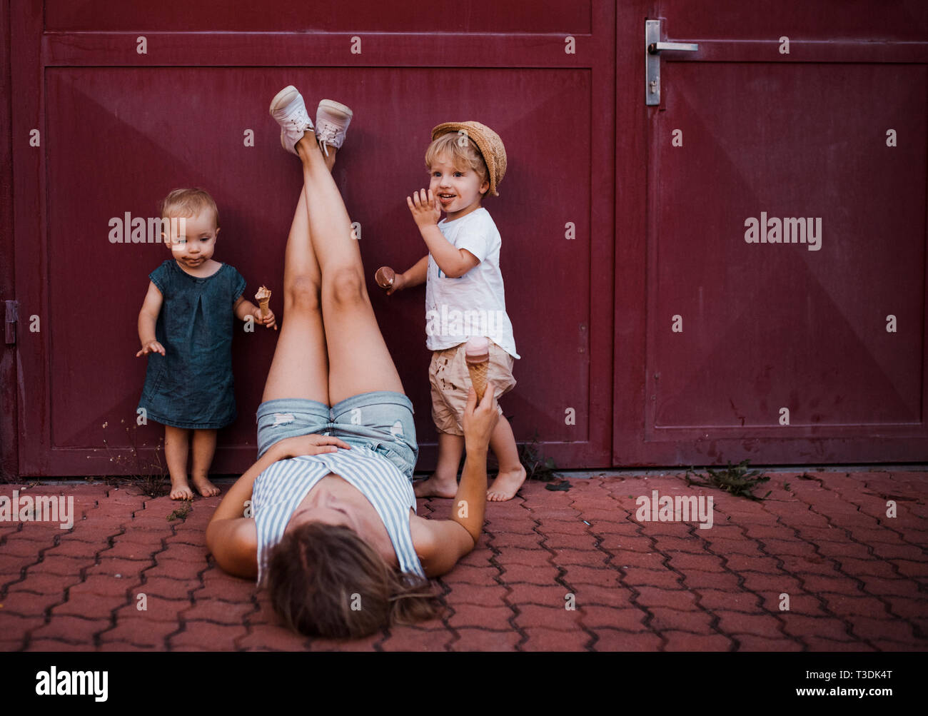 Une jeune mère de deux enfants tout-petits à l'extérieur en été, la consommation de crème glacée. Banque D'Images