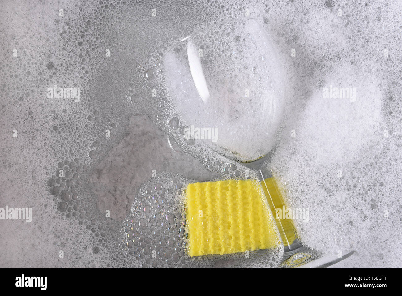 Portrait d'un égouttoir avec un seul verre de vin et d'une éponge jaune immergé dans de l'eau savonneuse. Banque D'Images