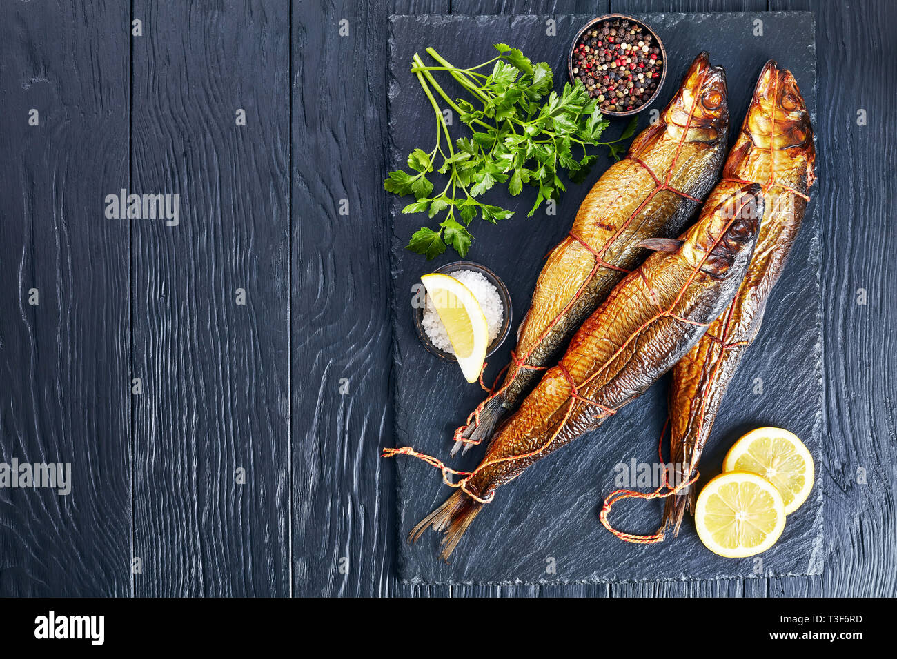 Ensemble de harengs fumés à chaud avec les tranches de citron, le persil et le poivre sur un plateau en ardoise noire sur une table en bois, vue de dessus, flatlay, copy space Banque D'Images