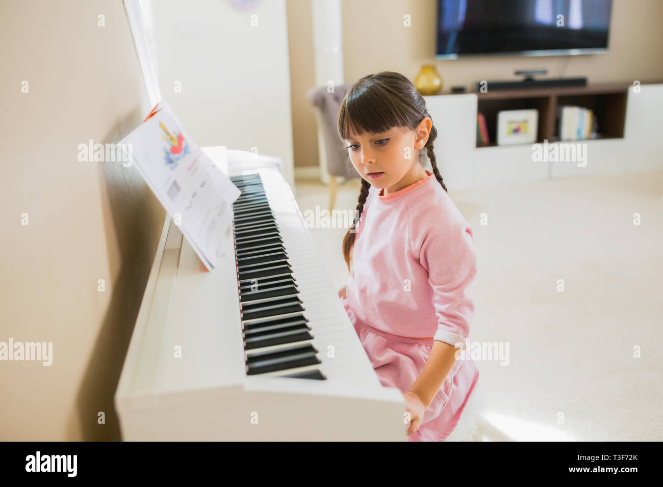 6-7 ans, fille joue un piano blanc à la maison. Banque D'Images