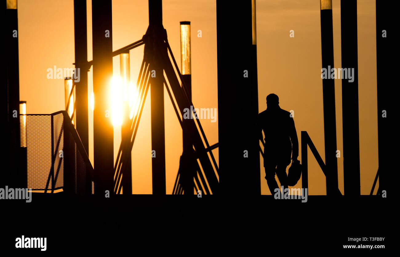 Hanovre, Allemagne. 09 avr, 2019. Un homme marche sur un pont à l'Expo Plaza avec un porte-documents au lever du soleil. Credit : Julian Stratenschulte/dpa/Alamy Live News Banque D'Images
