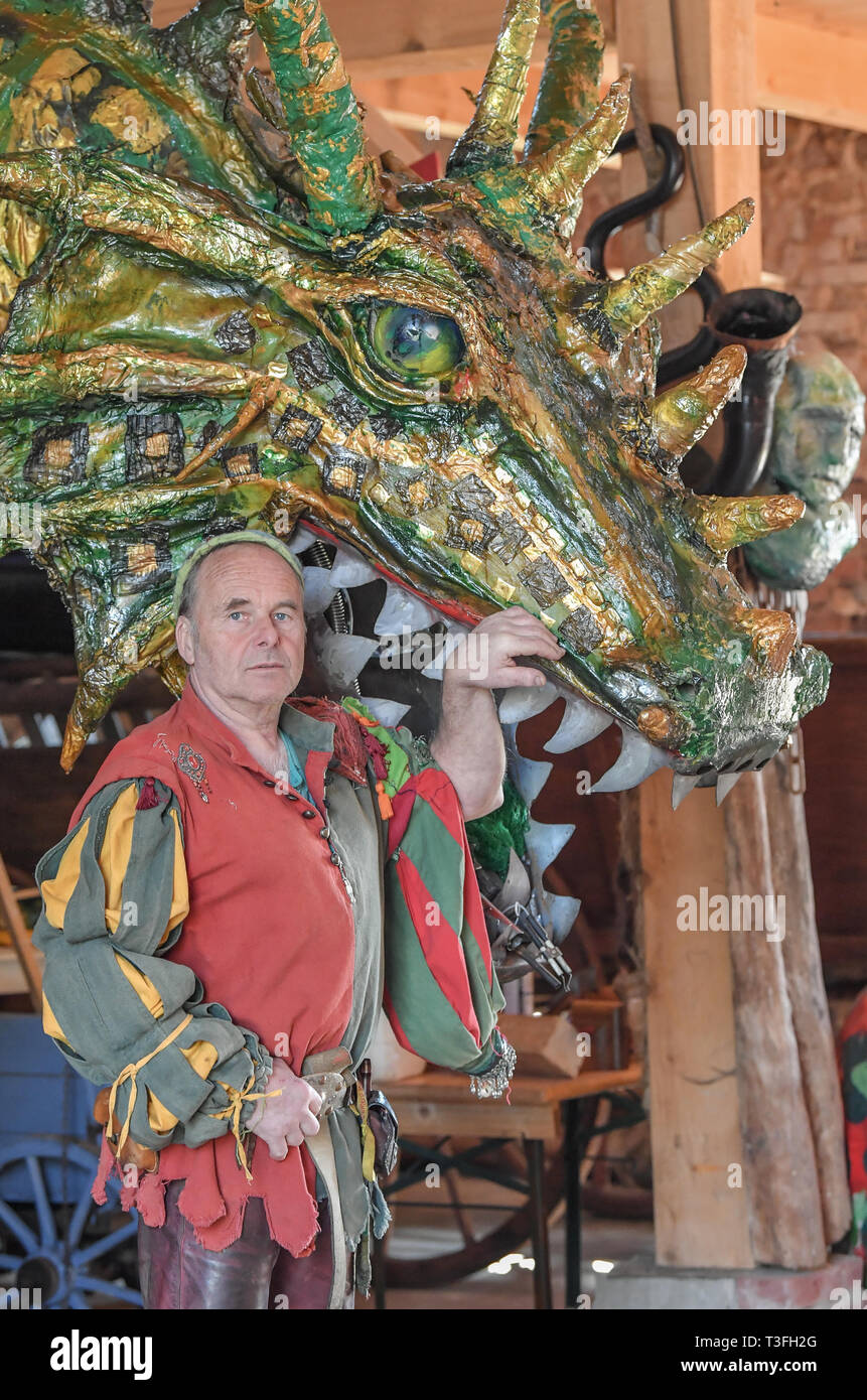 Golzow, Allemagne. Le 08 Avr, 2019. Streisand romain, musicien et artiste, se dresse en face d'un grand dragon figure dans une grange de sa Kulturhof. Le monastère de Pâques Festival en avant du fond de monastère de Chorin est devenu une institution et pour de nombreuses familles une excursion doit les jours fériés. Cette année, il y a la 30e édition. Il a été inventé par Roman Streisand, qui tire toujours les cordes avec son pilwut "bande médiéval'. Crédit : Patrick Pleul/dpa-Zentralbild/ZB/dpa/Alamy Live News Banque D'Images