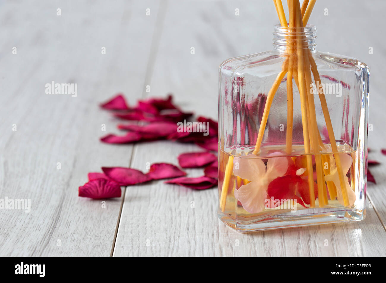 Avec diffuseur parfum dans un bocal en verre avec des pétales de rose sur un fond en bois gris Banque D'Images