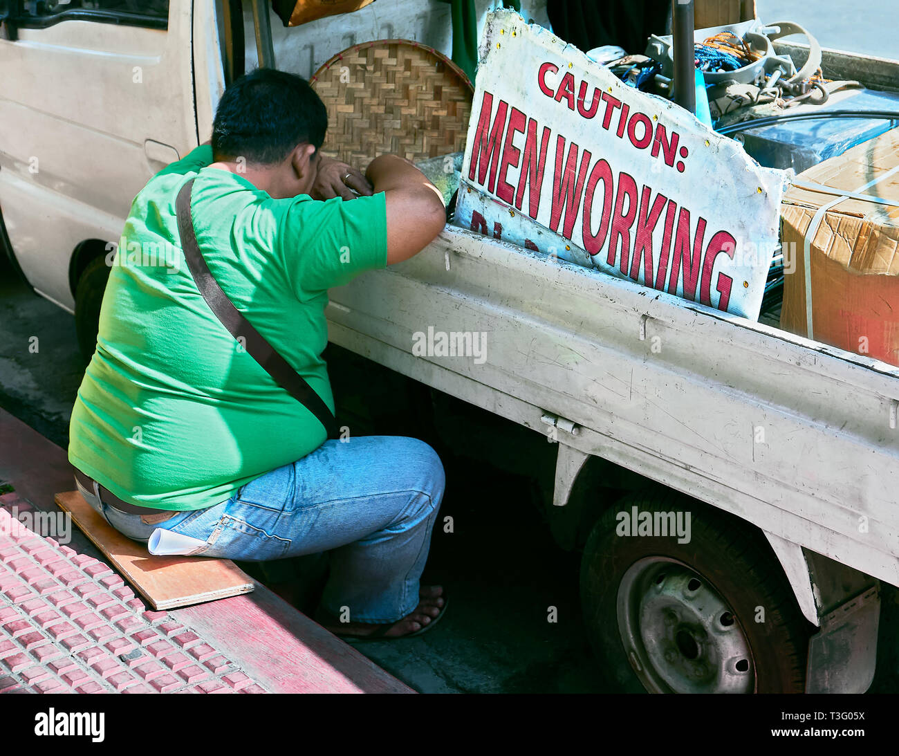 Manille, Philippines : l'excès de l'homme assis sur le plancher appuyé contre une voiture, dormir à côté de la signalisation "Attention, Travaux" Banque D'Images