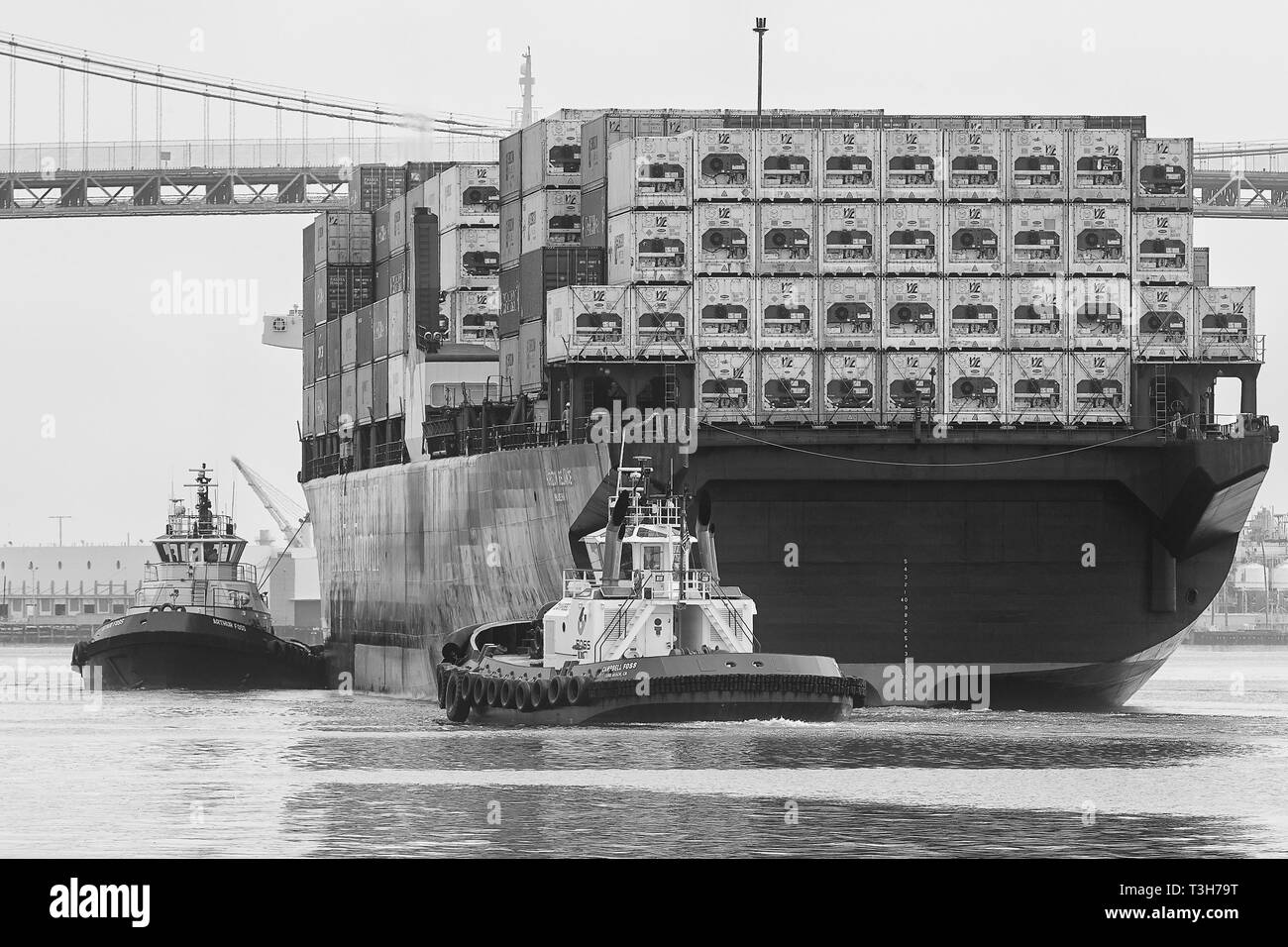 Photo en noir et blanc de remorqueurs guidant le porte-conteneurs HORIZON RELIANCE, sous le pont Vincent Thomas au port de Los Angeles, États-Unis Banque D'Images