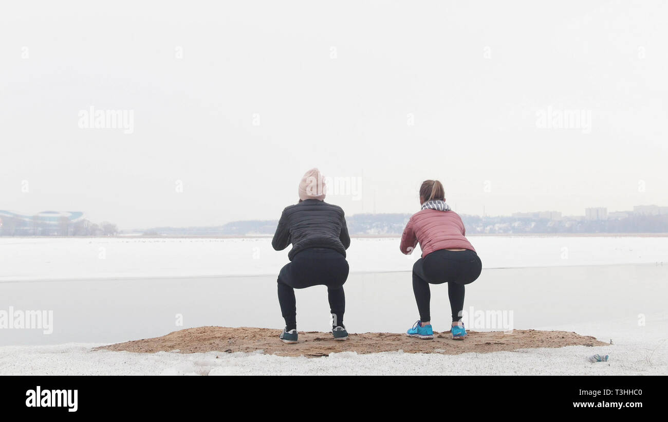 Deux femmes slim debout sur la plage enneigée et faisant s'accroupit Banque D'Images