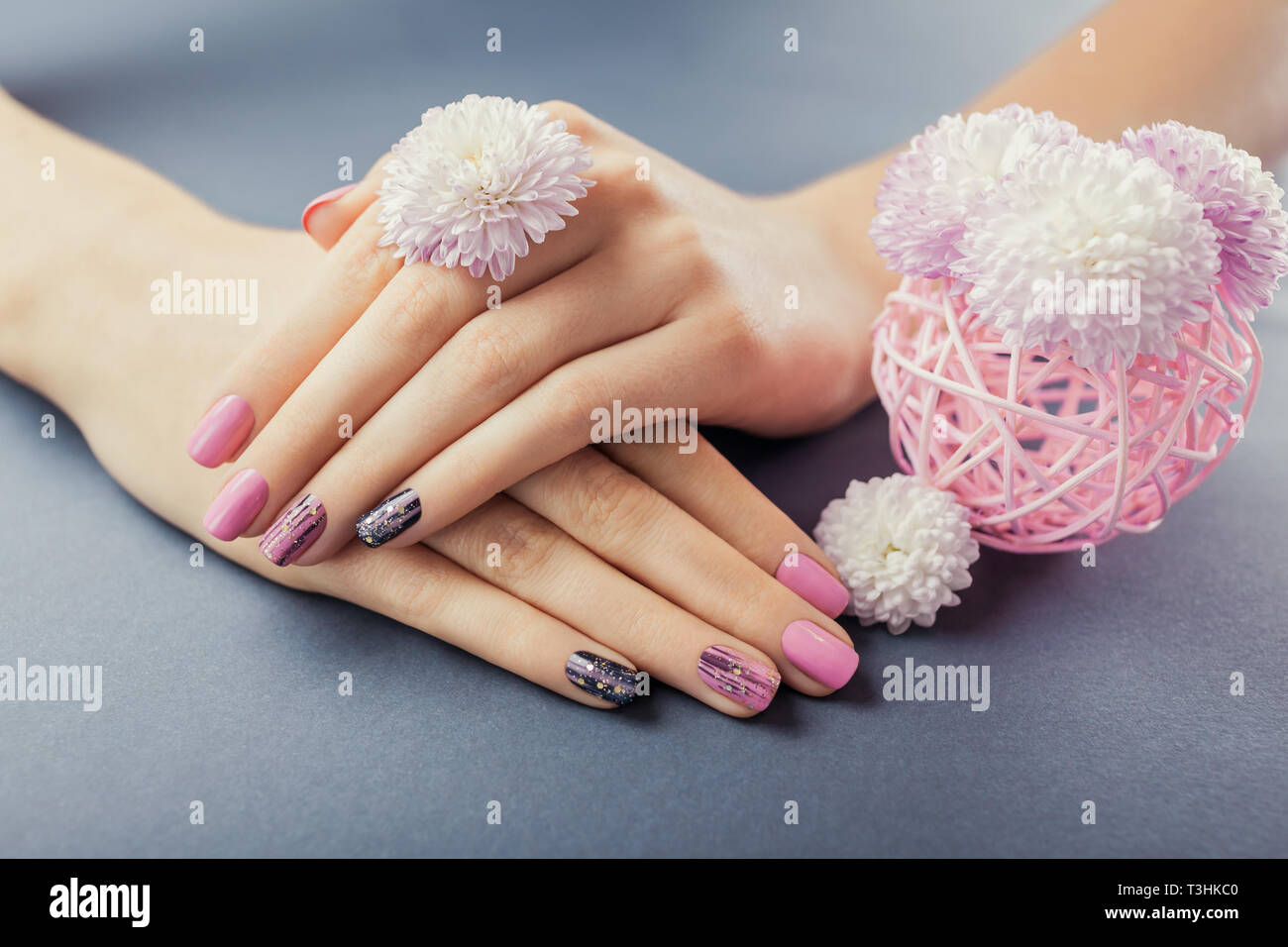 Manucure rose et noir sur les mains avec des fleurs sur fond gris. Nail art et design. Soins du corps Banque D'Images