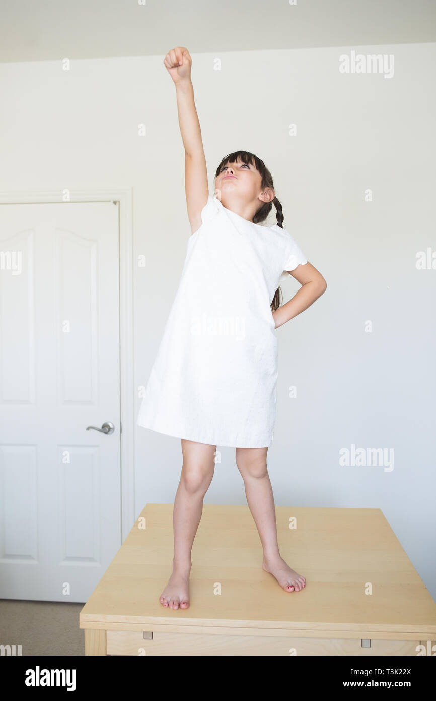 6-7 ans fille est sur le dessus de la table à la maison. Elle fait semblant de voler. Banque D'Images