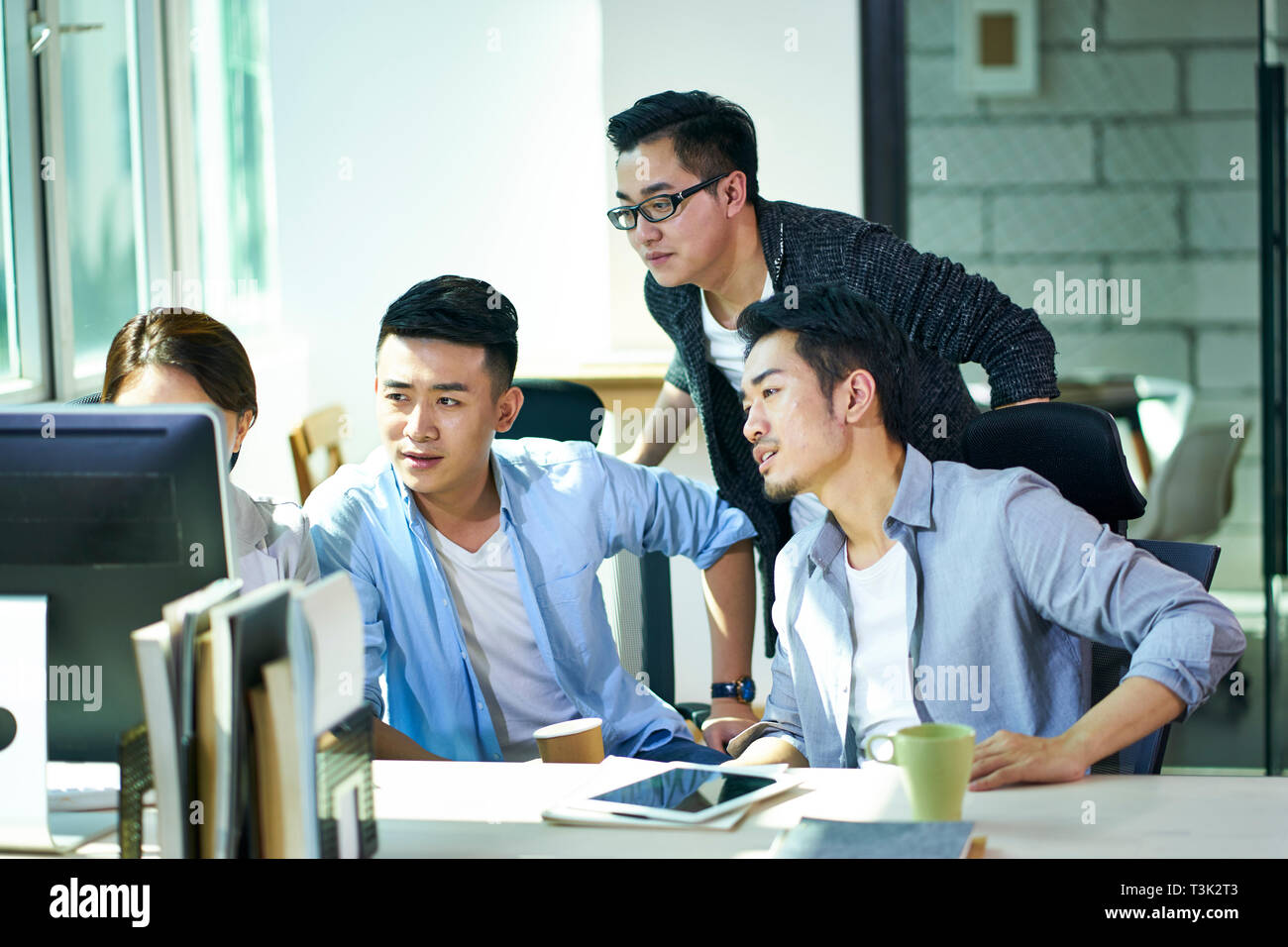 Quatre jeunes dirigeants de sociétés asiatiques travaillant ensemble discuter affaires plan à l'aide d'ordinateur de bureau en bureau. Banque D'Images