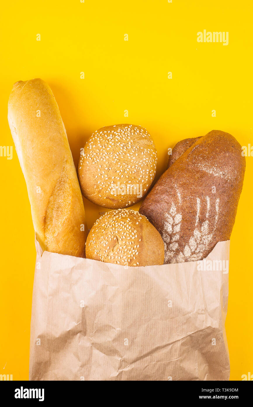 Pain frais, varié dans un sac en papier sur un fond jaune - blanc baguette, céréales et pain foncé buns au sésame. Haut de la vue, télévision lay Banque D'Images