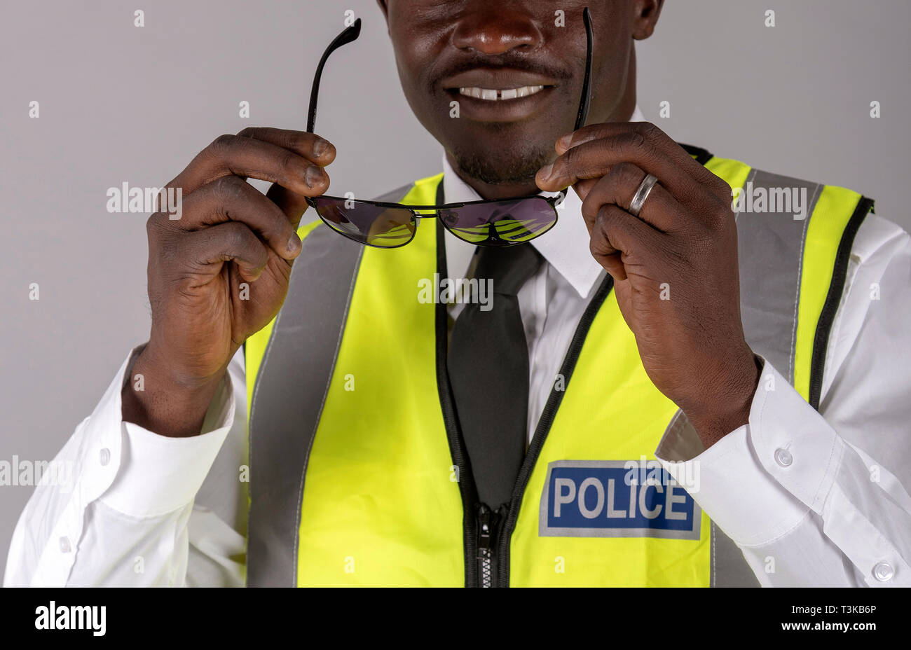 Portrait of a smiling agent de police en uniforme et tenant une paire de lunettes noires pour la protection des yeux. Banque D'Images