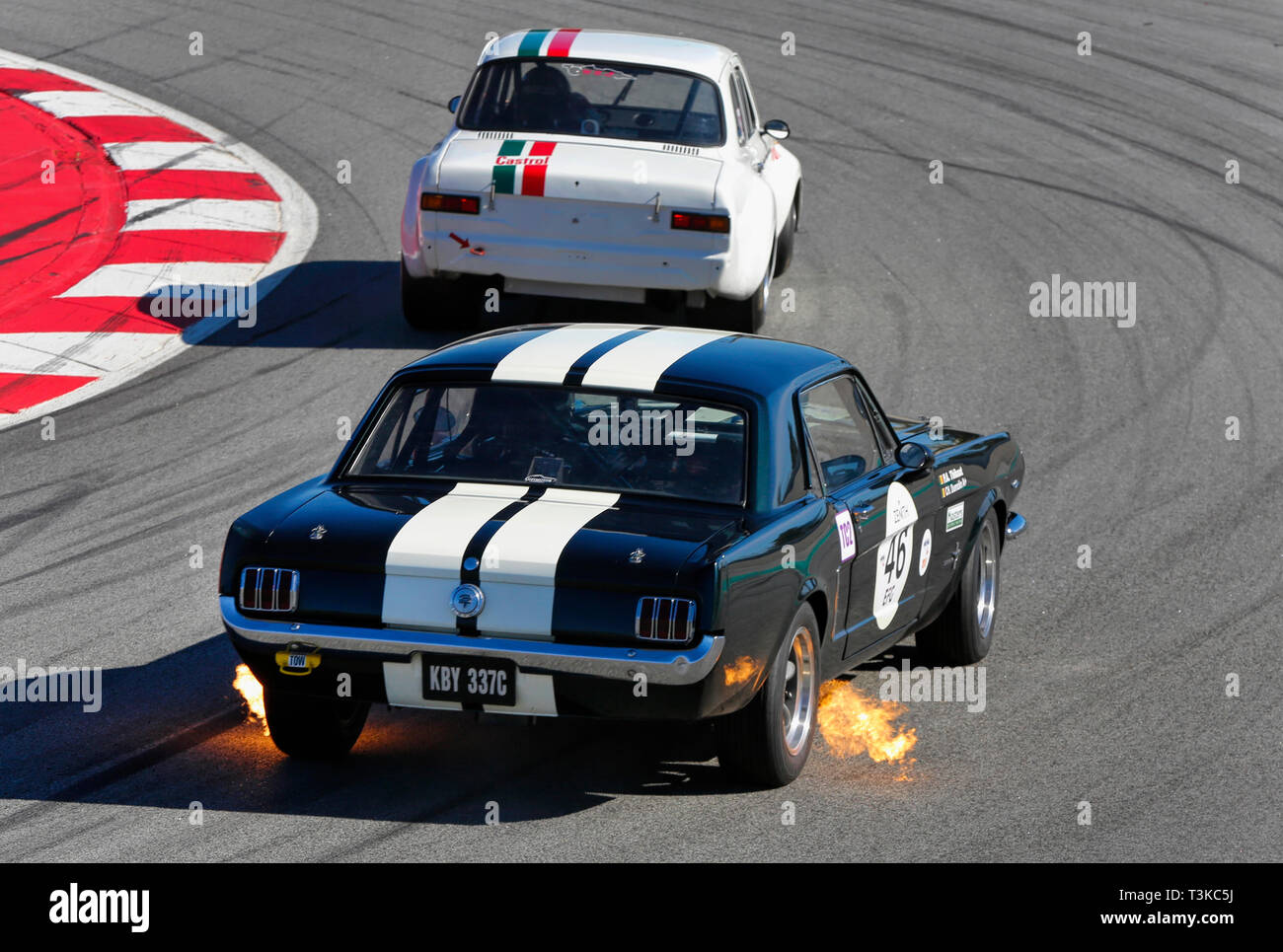 Voiture de course Ford Mustang historique crachant des flammes par les échappements latéraux tout en suivant une Alfa Romeo dans un virage du circuit Banque D'Images