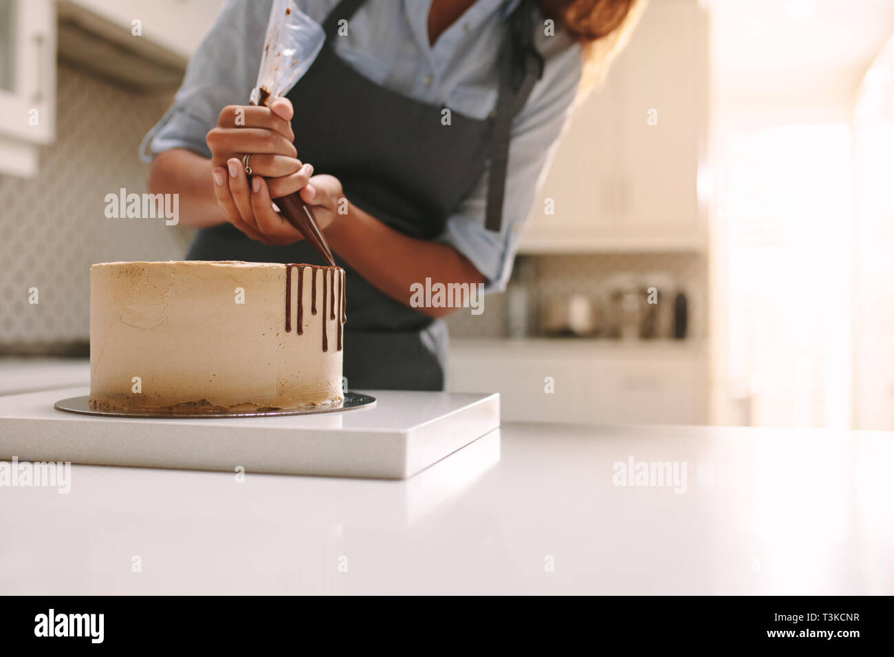 Tablier femme en décorant le gâteau avec du chocolat liquide. Chef pâtissier dans cuisine decorating cake au chocolat glaçage. Banque D'Images