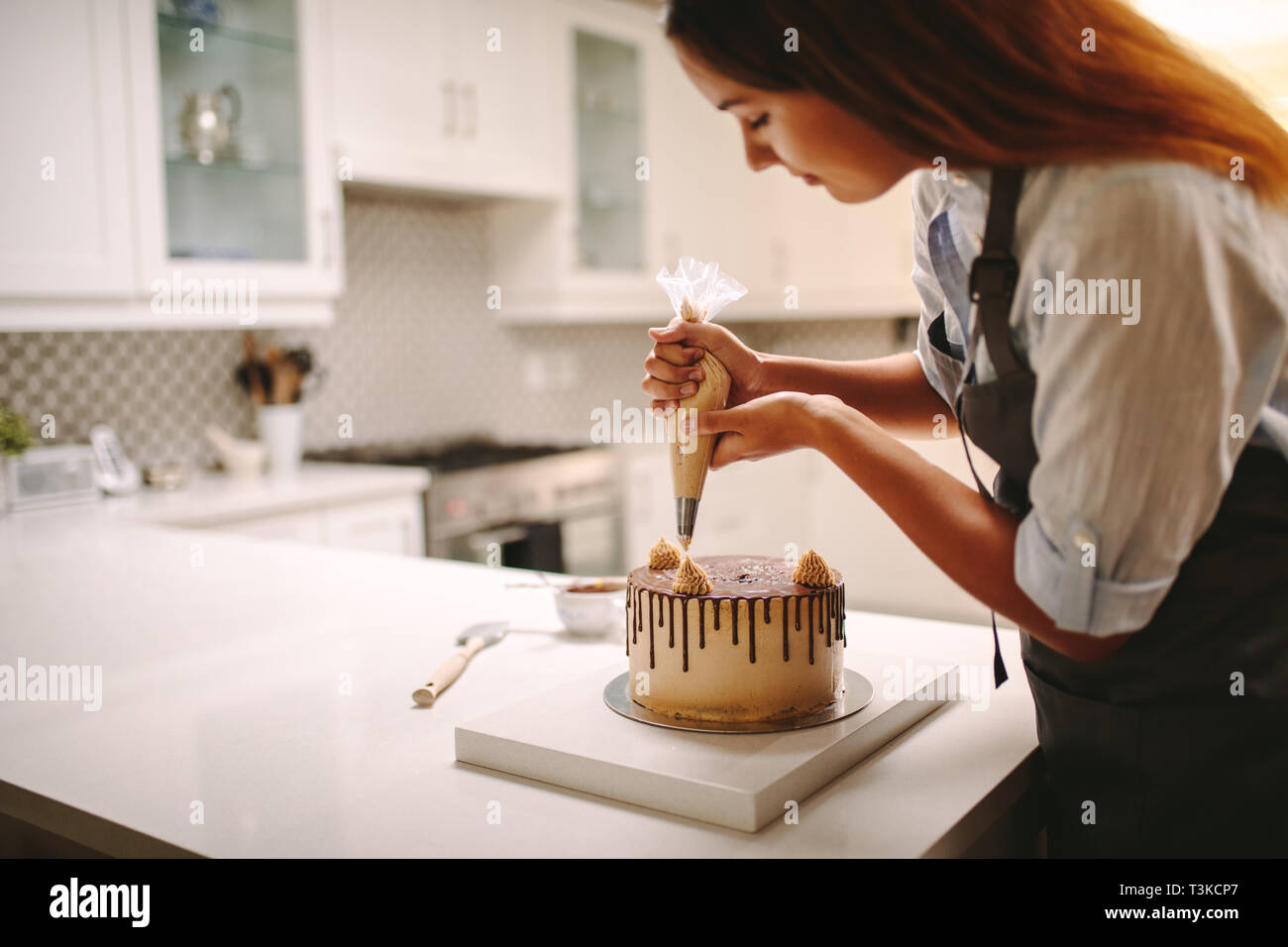 Femme pastry chef decorating cake au chocolat dans la cuisine. Femme portant un tablier decorating cake avec une poche à douille avec de la crème. Banque D'Images
