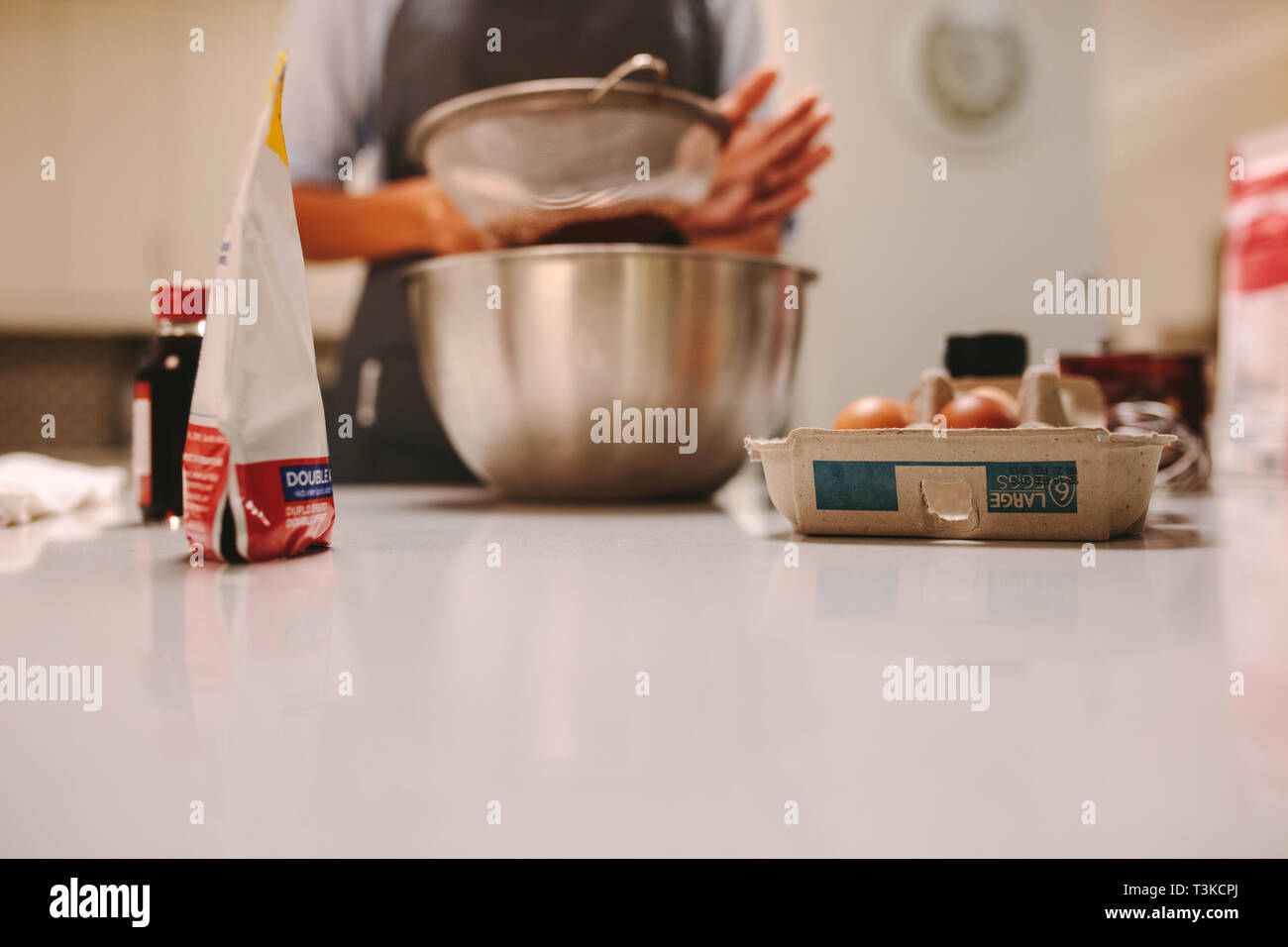 Ingrédients de cuisson sur comptoir de la cuisine avec femme sasser la farine dans le bol. Gâteau pâtissier préparation en cuisine. Banque D'Images