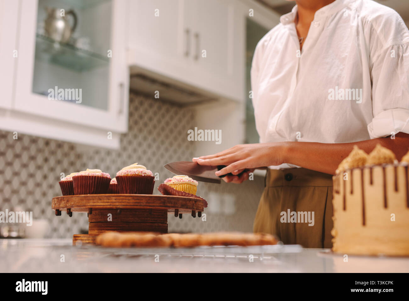 Femme chef de couper un petit gâteau sur planche de bois avec un couteau dans la cuisine. Confiseur femme travaillant dans la cuisine. Banque D'Images