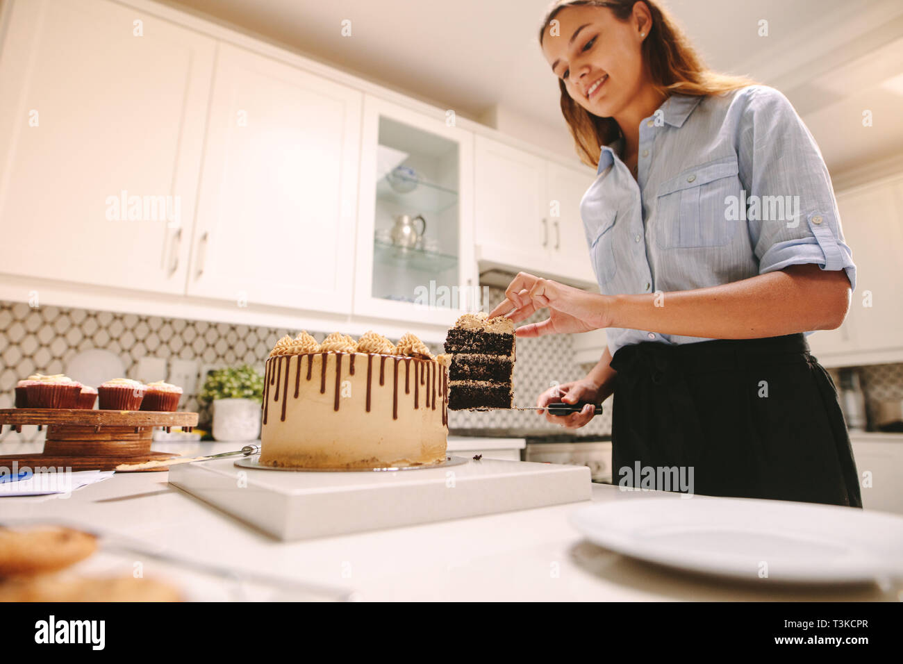 Chef de prendre une tranche de gâteau à la plaque avec un couteau. Femme pâtissier dans la cuisine. Banque D'Images