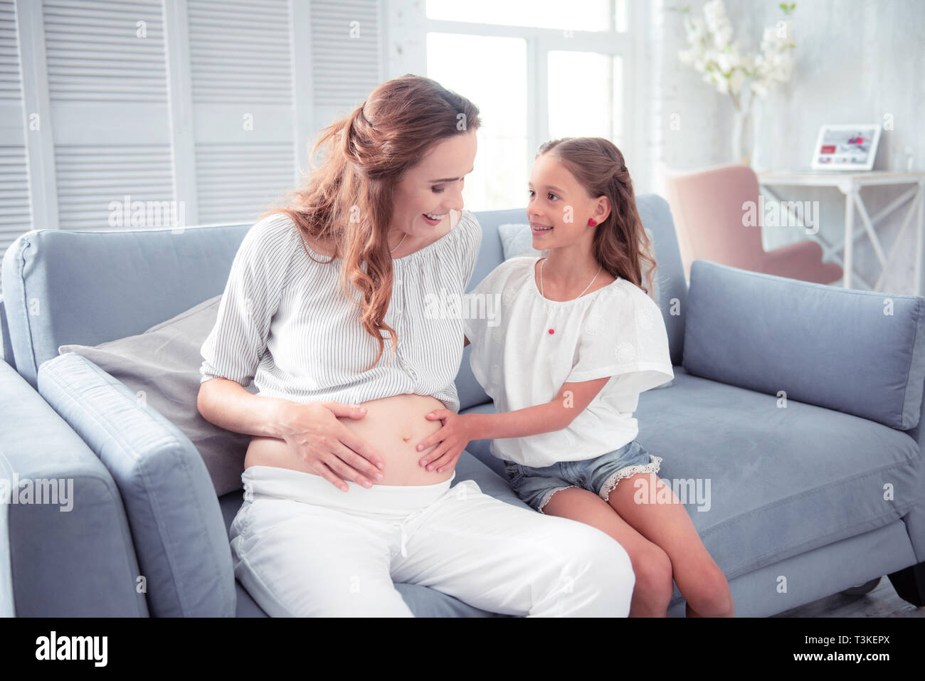 Mother smiling alors que sa fille aînée de toucher son ventre enceinte Banque D'Images
