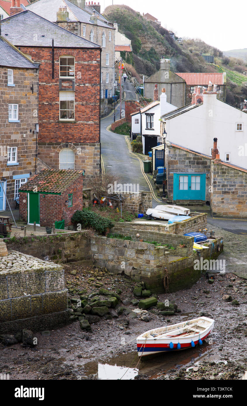 Bateau construit à clins à marée basse et maisons de Staithes, un village traditionnel de pêcheurs et station balnéaire sur la côte du Yorkshire du Nord, Angleterre, Royaume-Uni. Banque D'Images