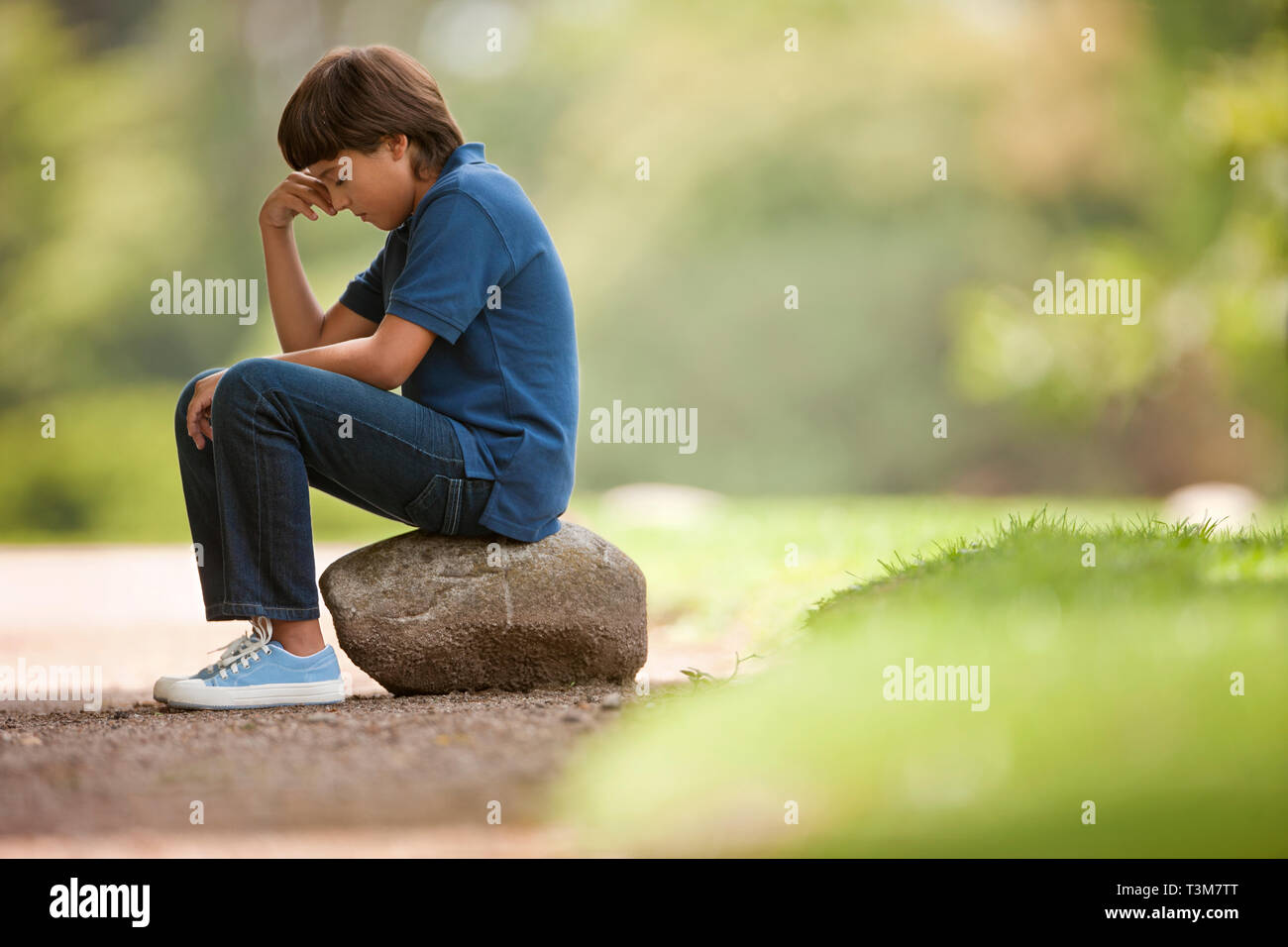 Malheureusement garçon est assis sur un rocher sur un chemin dans un parc. Banque D'Images