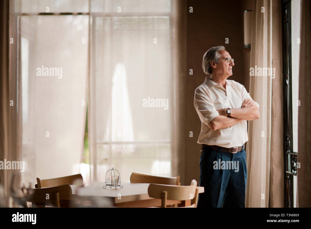 Man regarde par une fenêtre, les bras croisés. Banque D'Images