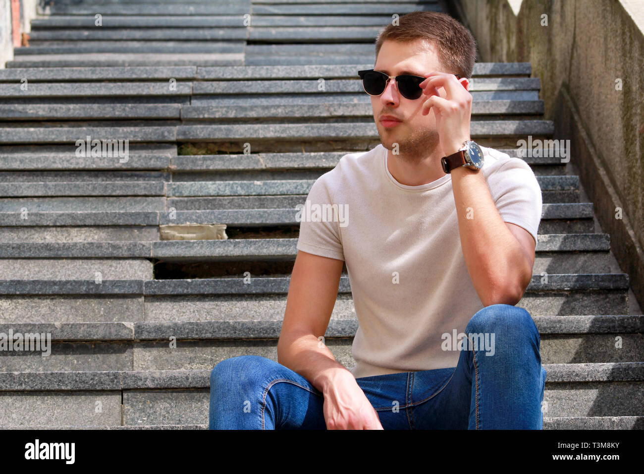 Homme assis seul sur mesures. Beau garçon avec des lunettes de soleil.  Modèle masculin pose pour la prise de vue, assis sur de vieux escaliers.  Portrait de mec cool assis Photo Stock -