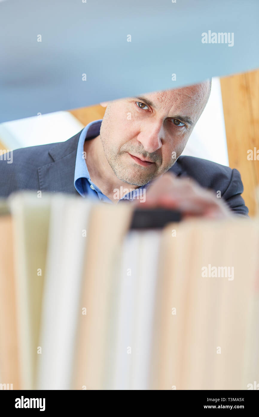 L'homme est à la recherche d'un livre sur une étagère de bibliothèque ou librairie Banque D'Images