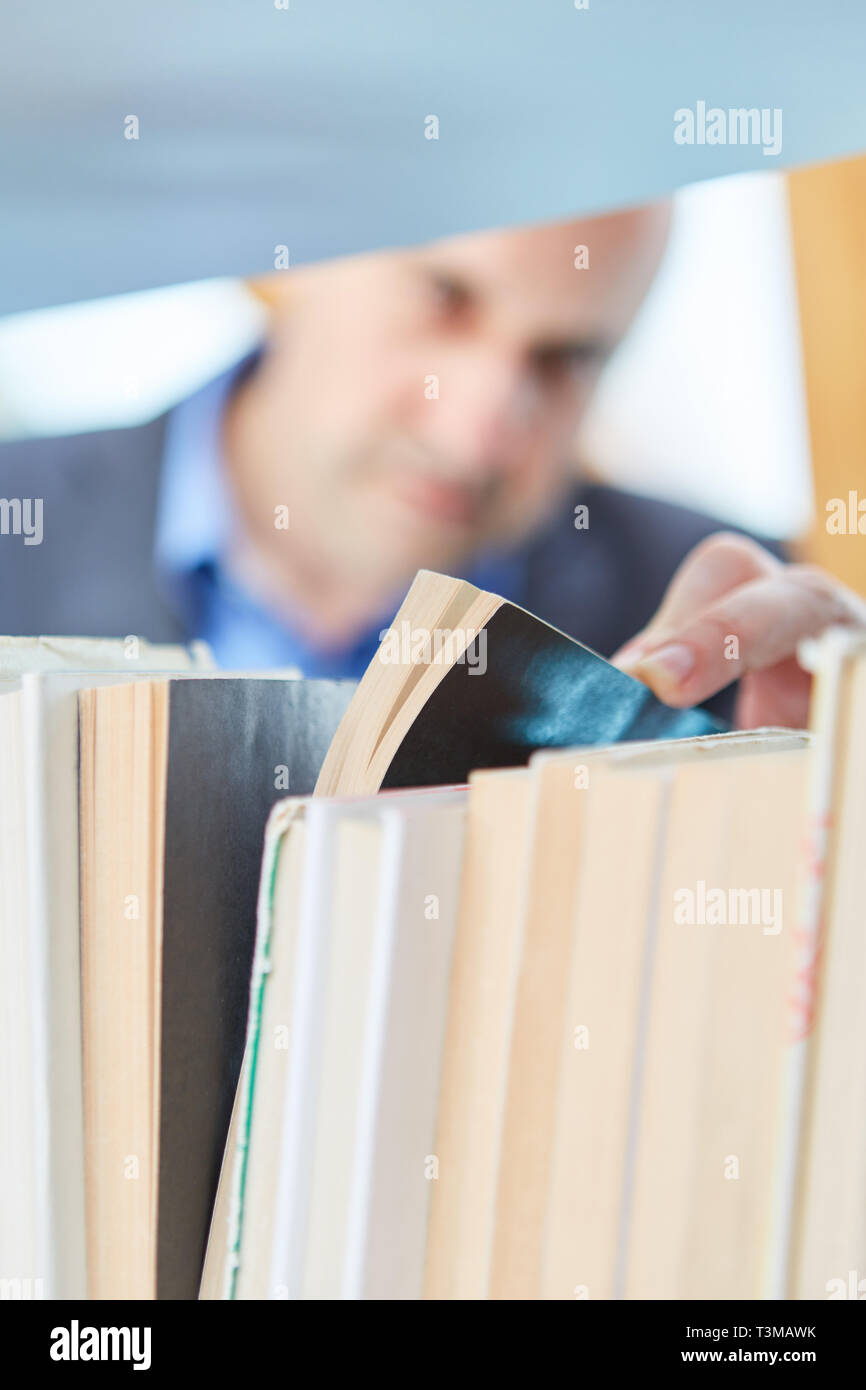 L'homme comme un lecteur est à la recherche d'un livre à louer sur l'étagère d'une bibliothèque ou à la librairie Banque D'Images