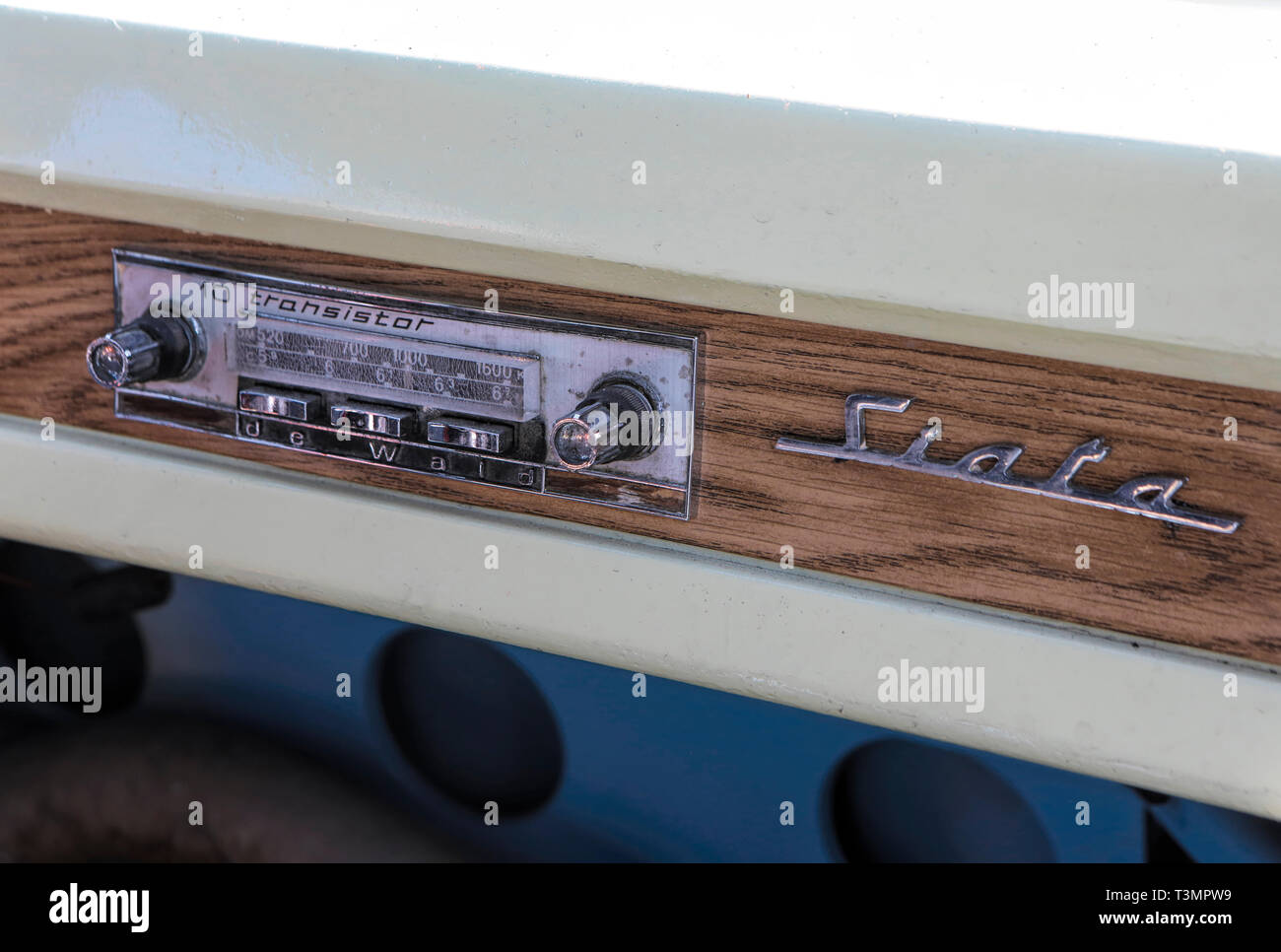 Vue détaillée d'un tuner radio à transistor vintage et d'un badge chromé Siata en script monté sur la garniture en grain de bois du tableau de bord d'une voiture Siata classique. Banque D'Images
