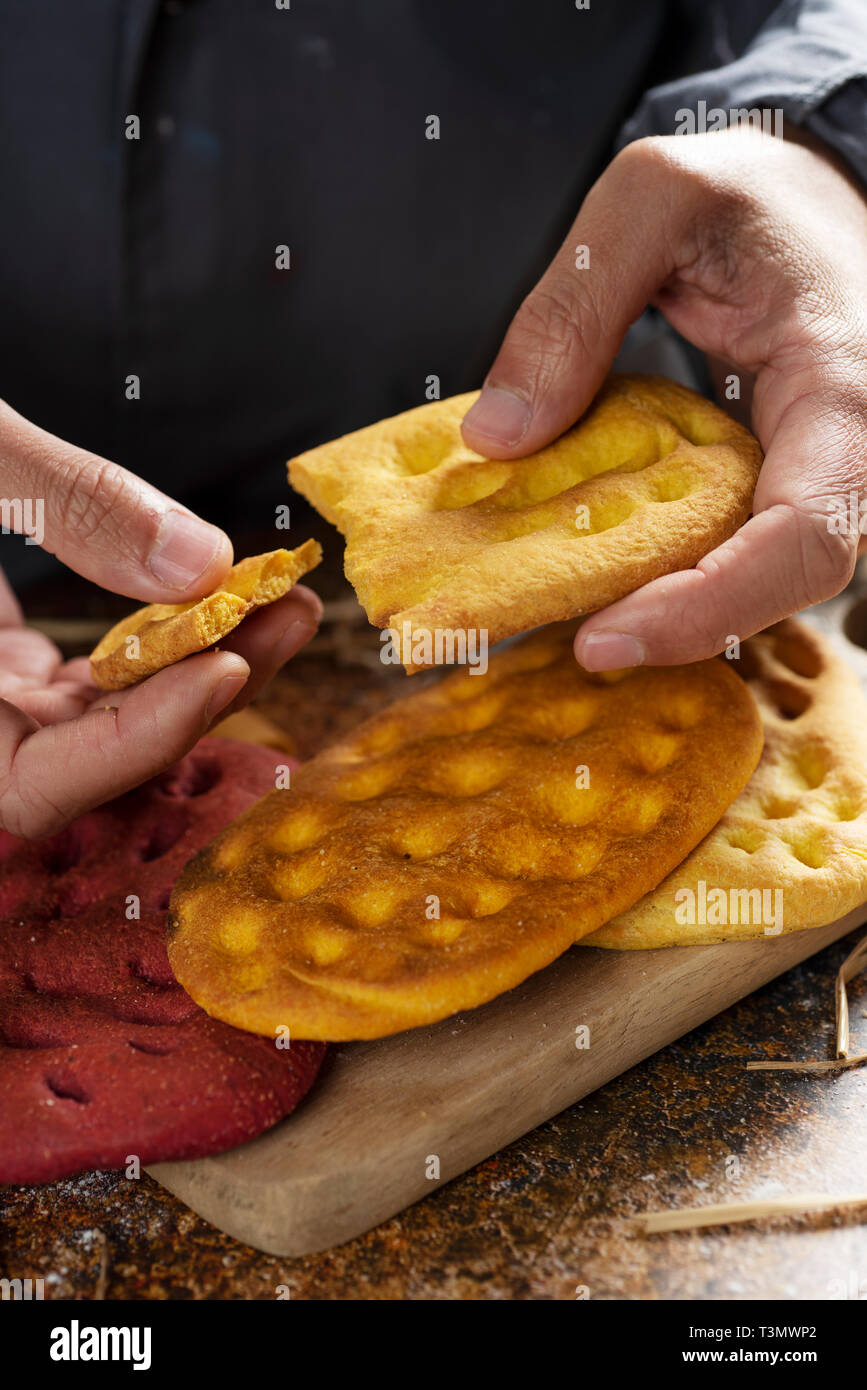 Un homme libre de la division d'un morceau d'une focaccia italienne, et d'autres différents focaccia, à la citrouille, la carotte et la betterave, sur une table en bois rustique Banque D'Images