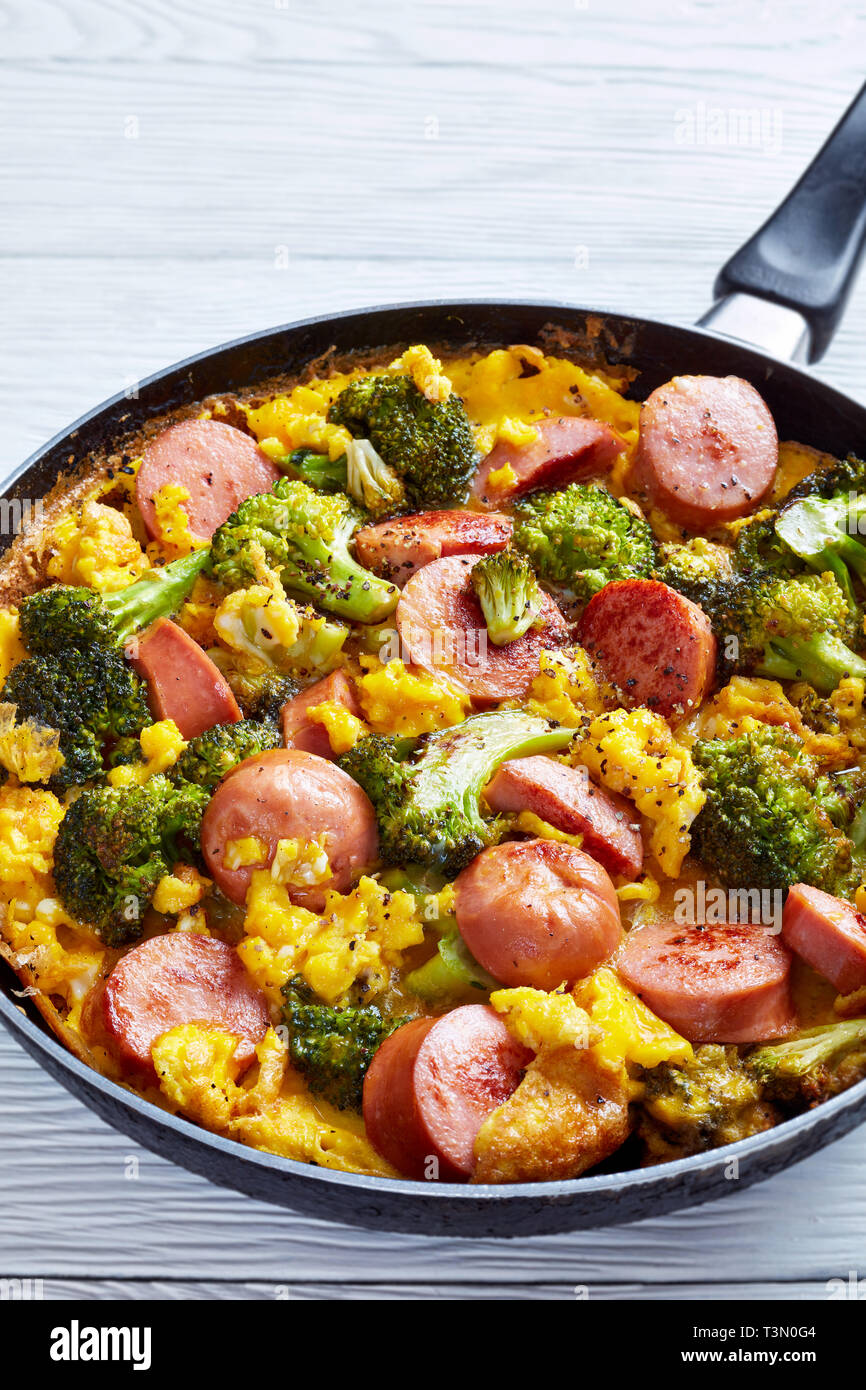 Délicieux chaud omelette aux brocolis et les saucisses dans une poêle saupoudrée de poivre fraîchement moulu, vue verticale de ci-dessus, Banque D'Images