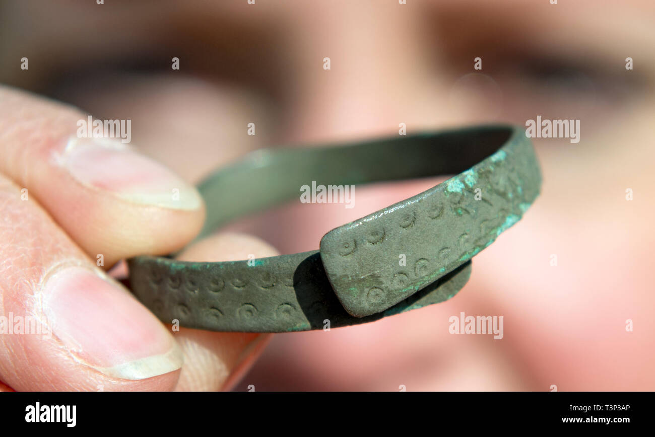 Griebo, Allemagne. Apr 11, 2019. Xandra Dalidowski, directeur d'excavation, montre un bracelet en bronze d'origine romaine sur un chantier de fouilles près de Griebo. Les archéologues ont découvert un site de règlement ici qui a des milliers d'années. Il y a 2450 ans la production de bijoux et d'outils a commencé ici. Ceci est démontré par la proximité des fosses, qui ont été utilisés comme foyer de fosses, puits et fosses à forger la production. La fusion et la transformation du fer a également eu lieu ici. Credit : Hendrik Schmidt/dpa-Zentralbild/ZB/dpa/Alamy Live News Banque D'Images