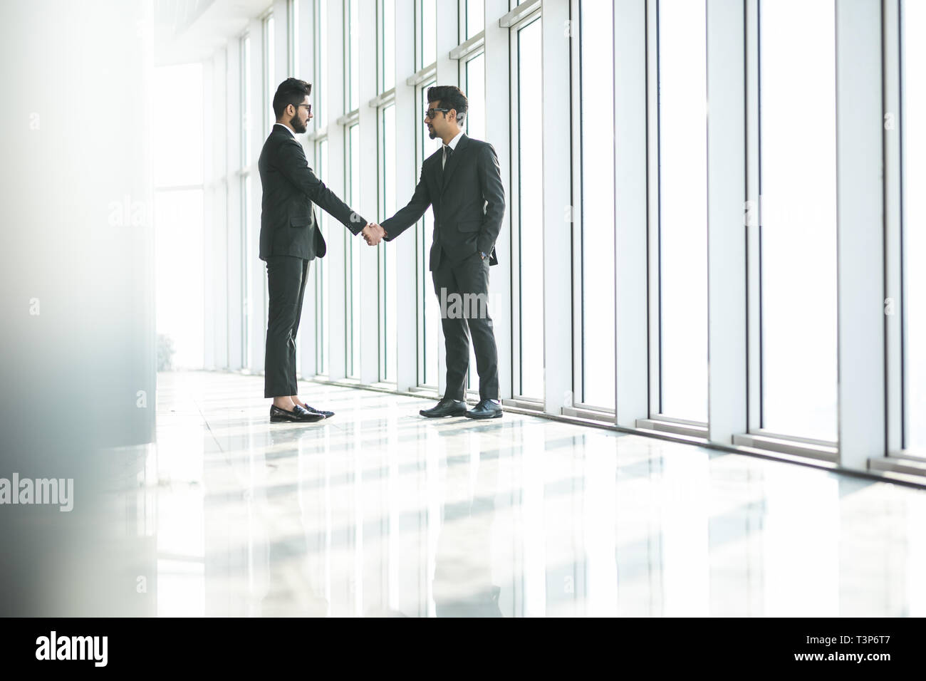 Deux indian businessman standing at grande fenêtre avec paysage urbain, confident business partners handshaking in office. Vue de côté Banque D'Images