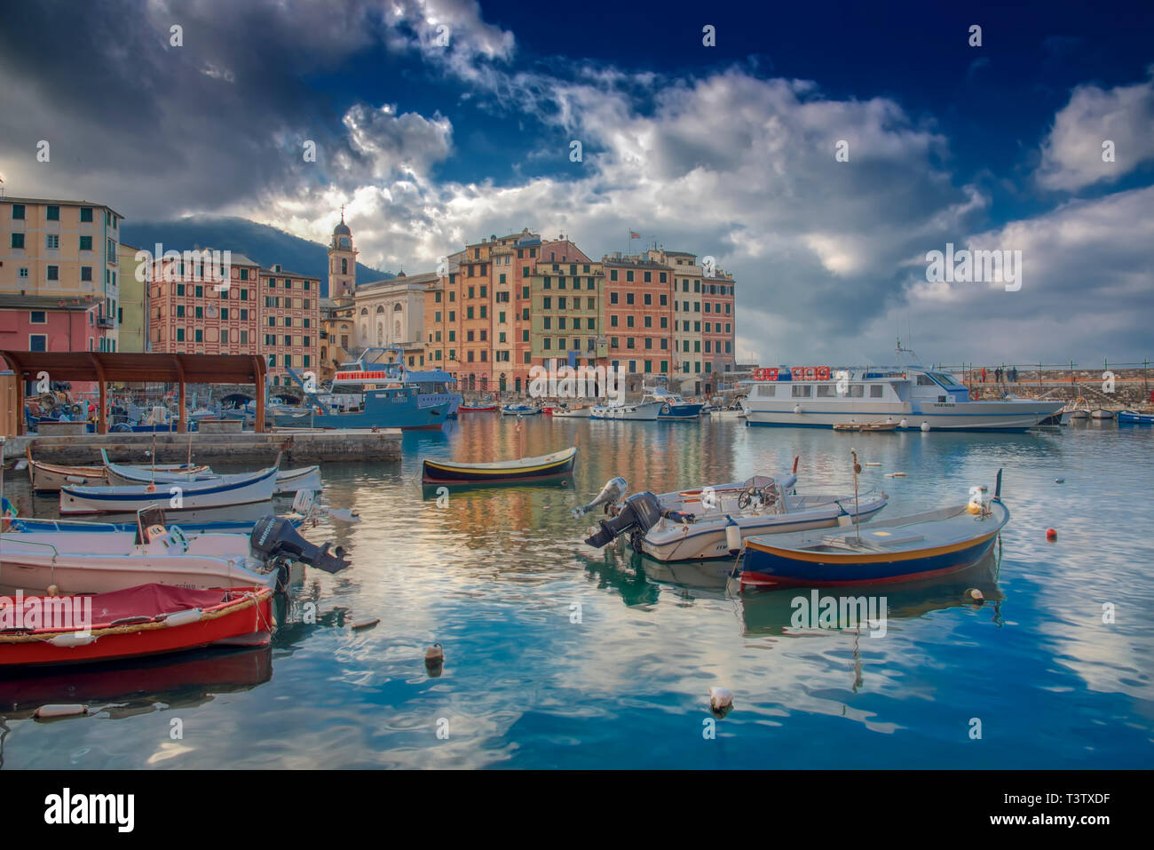 Scène portuaire paisible à Porticciolo di Camogli, ligurie, italie avec bateaux amarrés et bâtiments colorés sous un ciel nuageux ciel bleu Banque D'Images