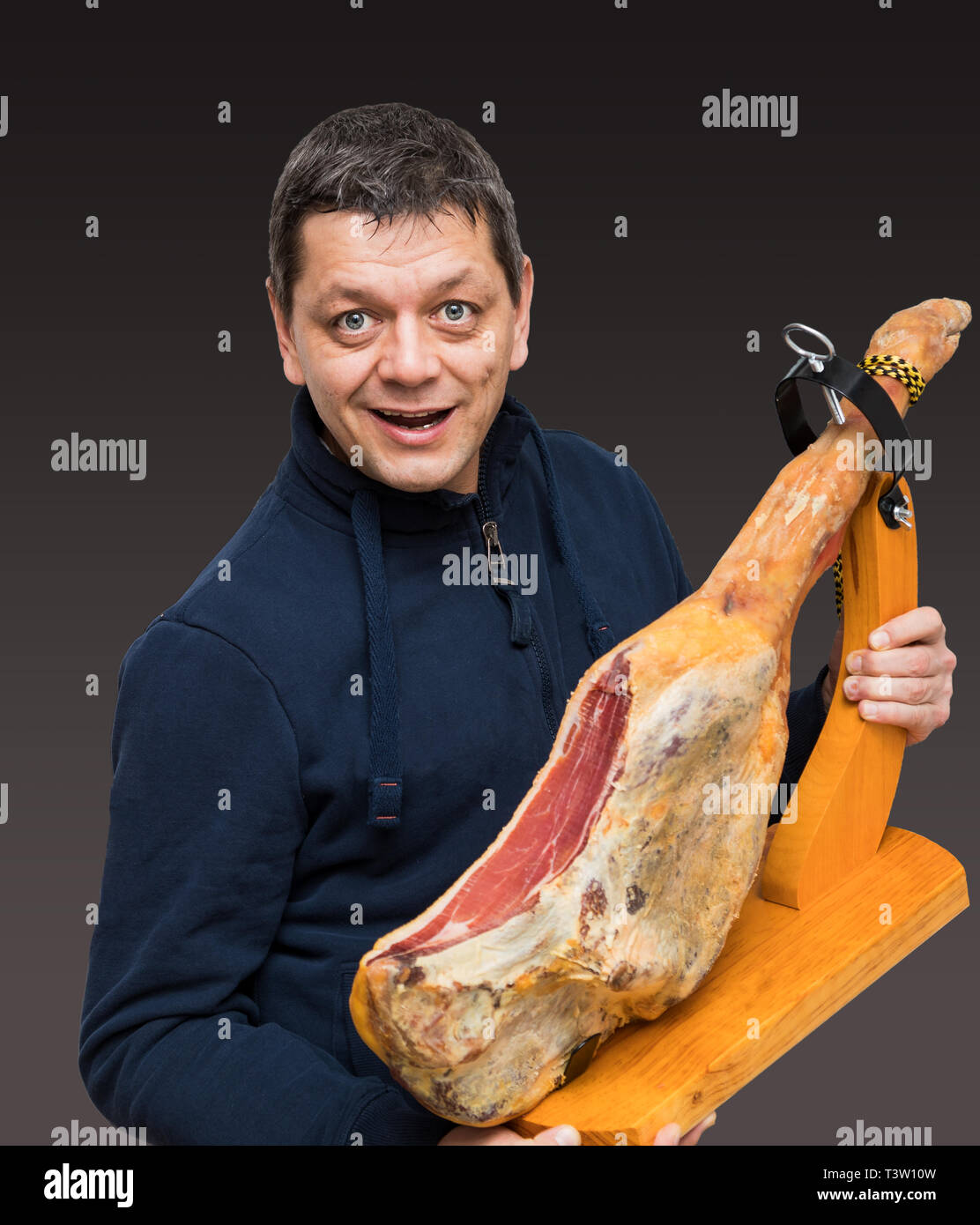 L'homme est titulaire d'un jambon Serrano espagnol sur la cuisse avec support en bois Banque D'Images