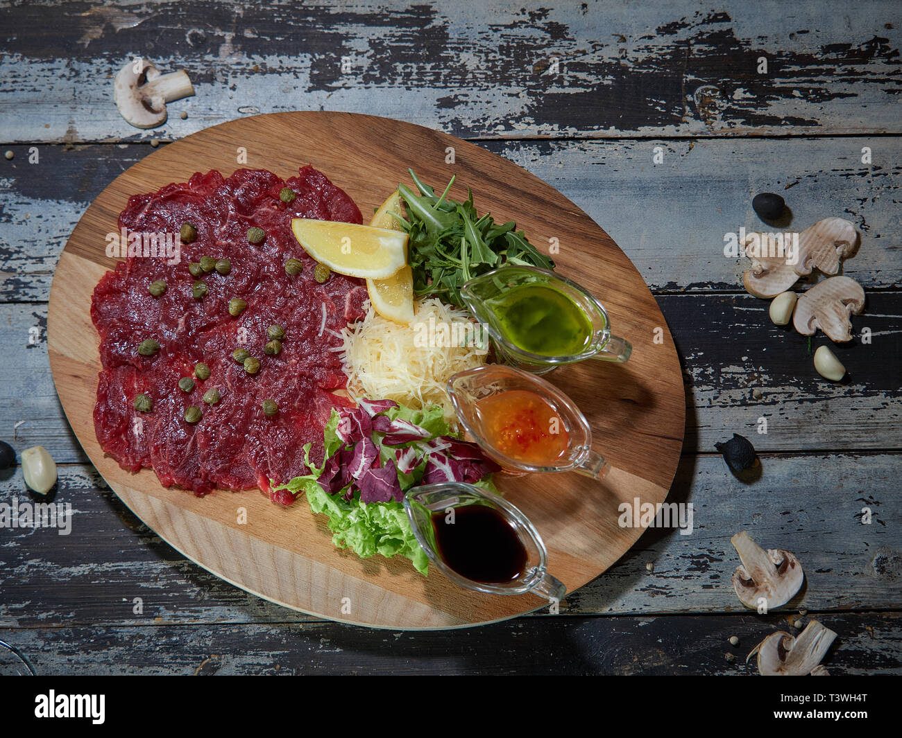 Un grand morceau de viande de b oe uf cru est servi sur une table, sur un plateau en bois avec des sauces pour la viande. Banque D'Images